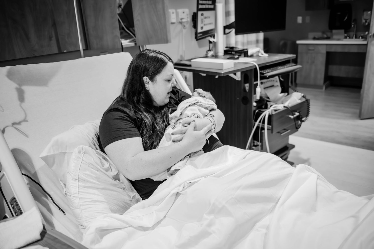 A peaceful hospital scene shows a parent cradling their newborn baby while resting in a medical bed.
