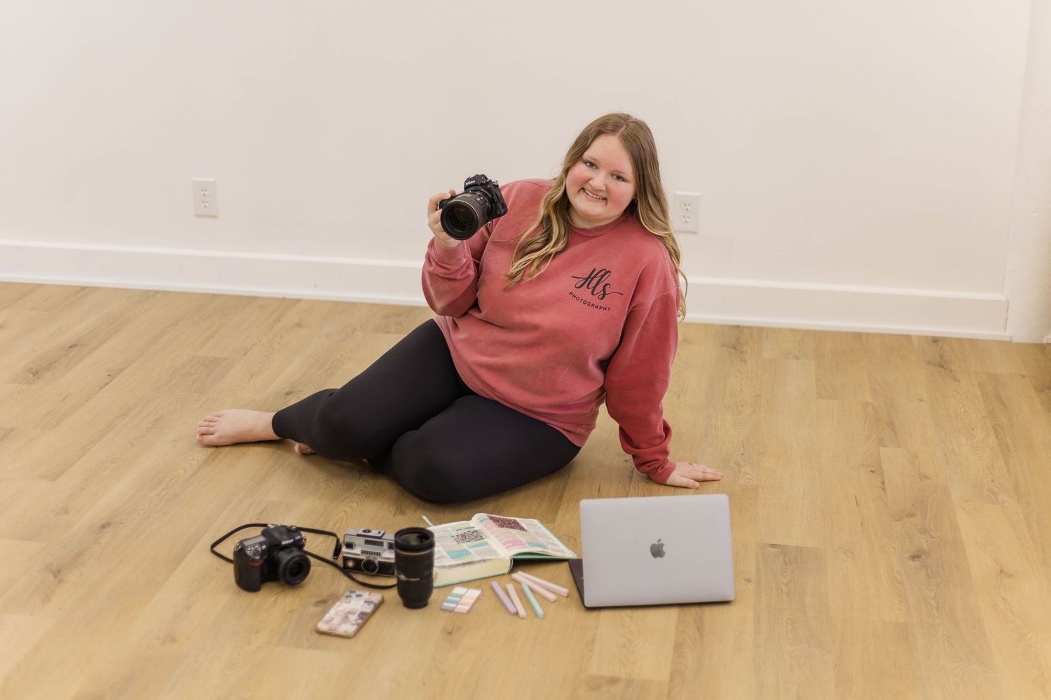 Person relaxing on wooden floor with laptop and photography equipment.