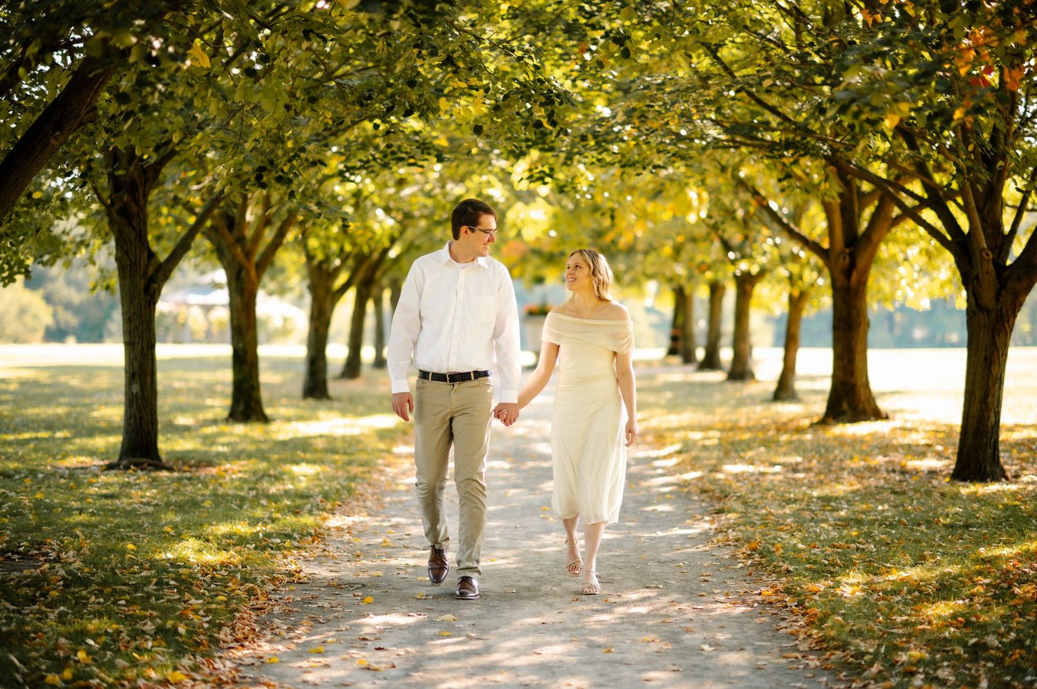 A couple walks hand in hand through a tree-lined path during golden hour.