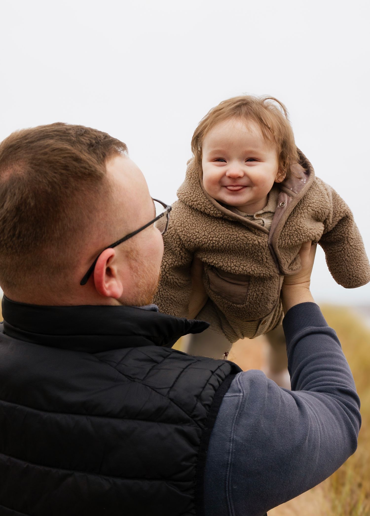 Dad lifting smiling baby in the air during a warm, natural lifestyle photoshoot