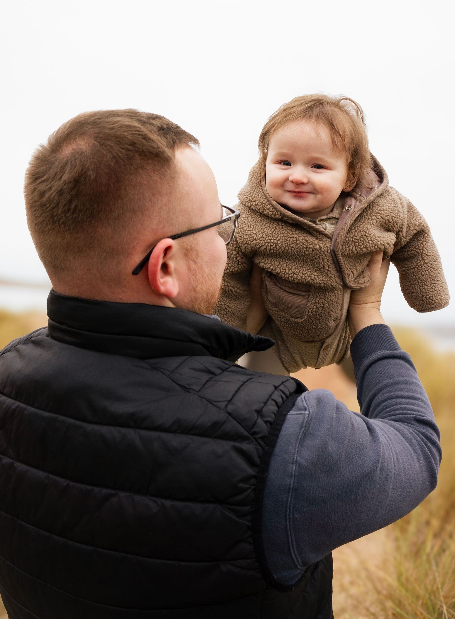 Dad lifting smiling baby in the air during a warm, natural lifestyle photoshoot