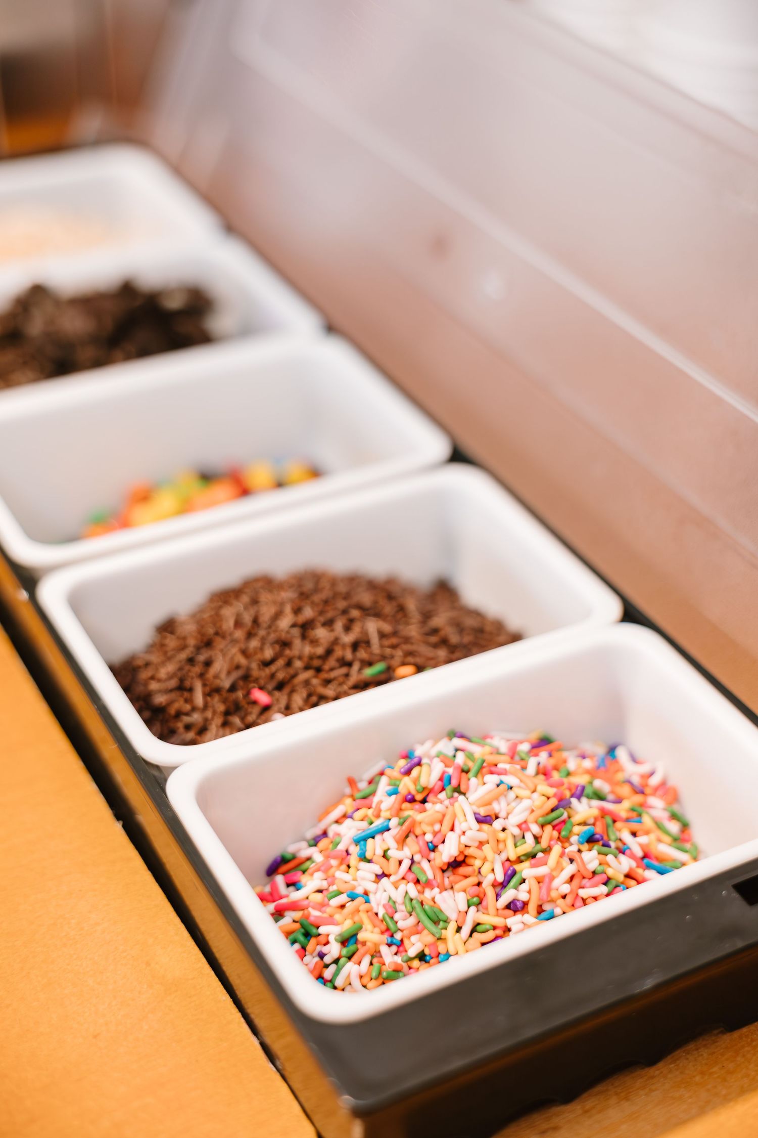 Ice cream topping station with colorful sprinkles and chocolate toppings in white containers.