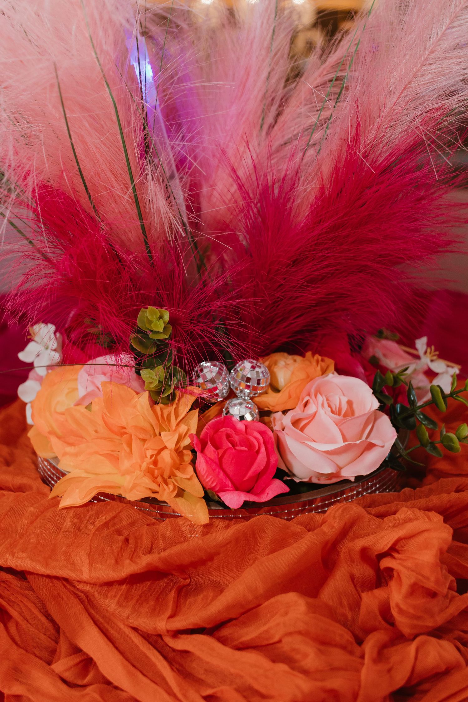 Floral centerpiece with pink pampas grass, orange and pink roses, and disco ball accents.