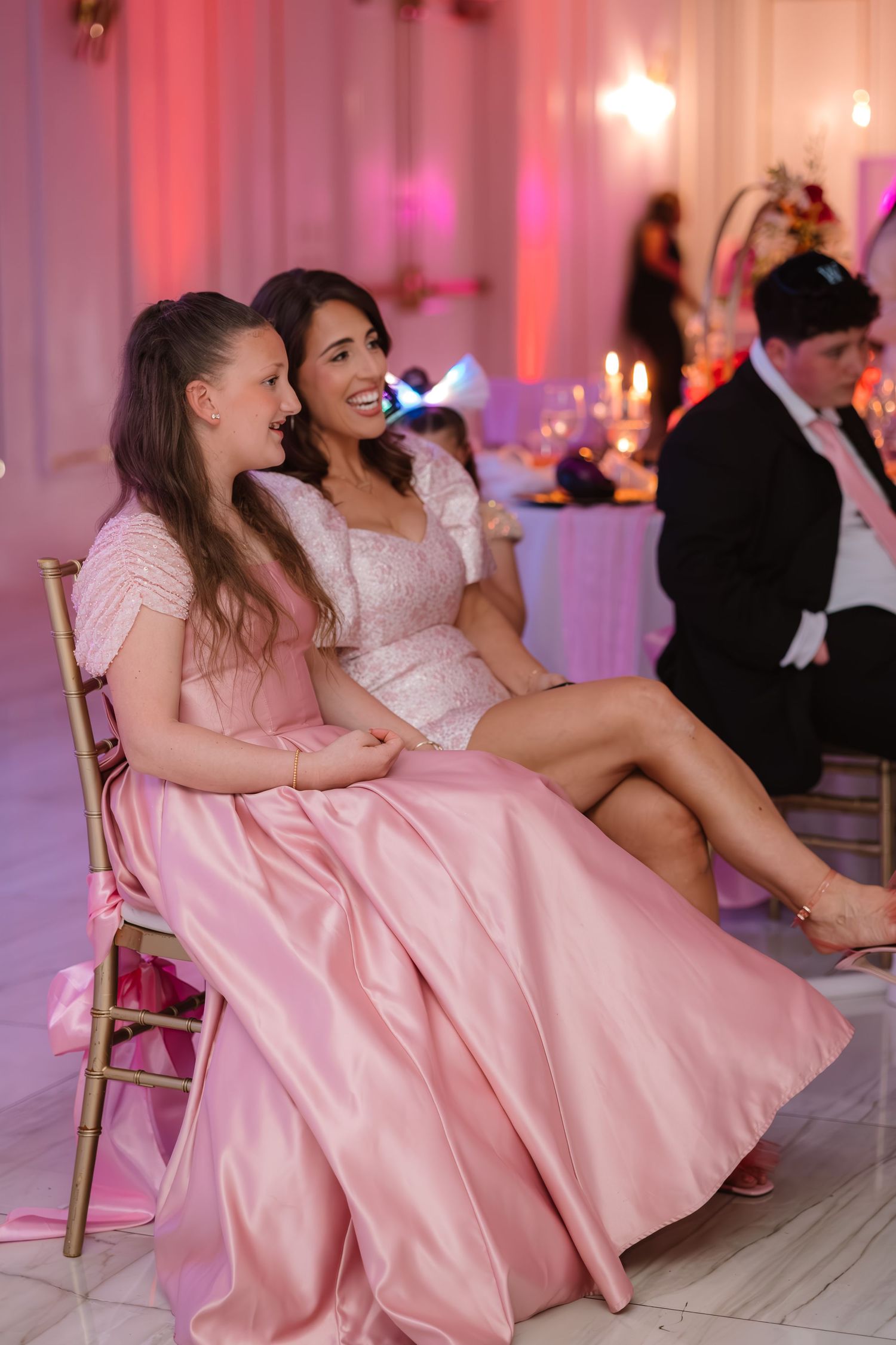 Two girls in pink dresses laughing together at an elegant pink-themed party event.