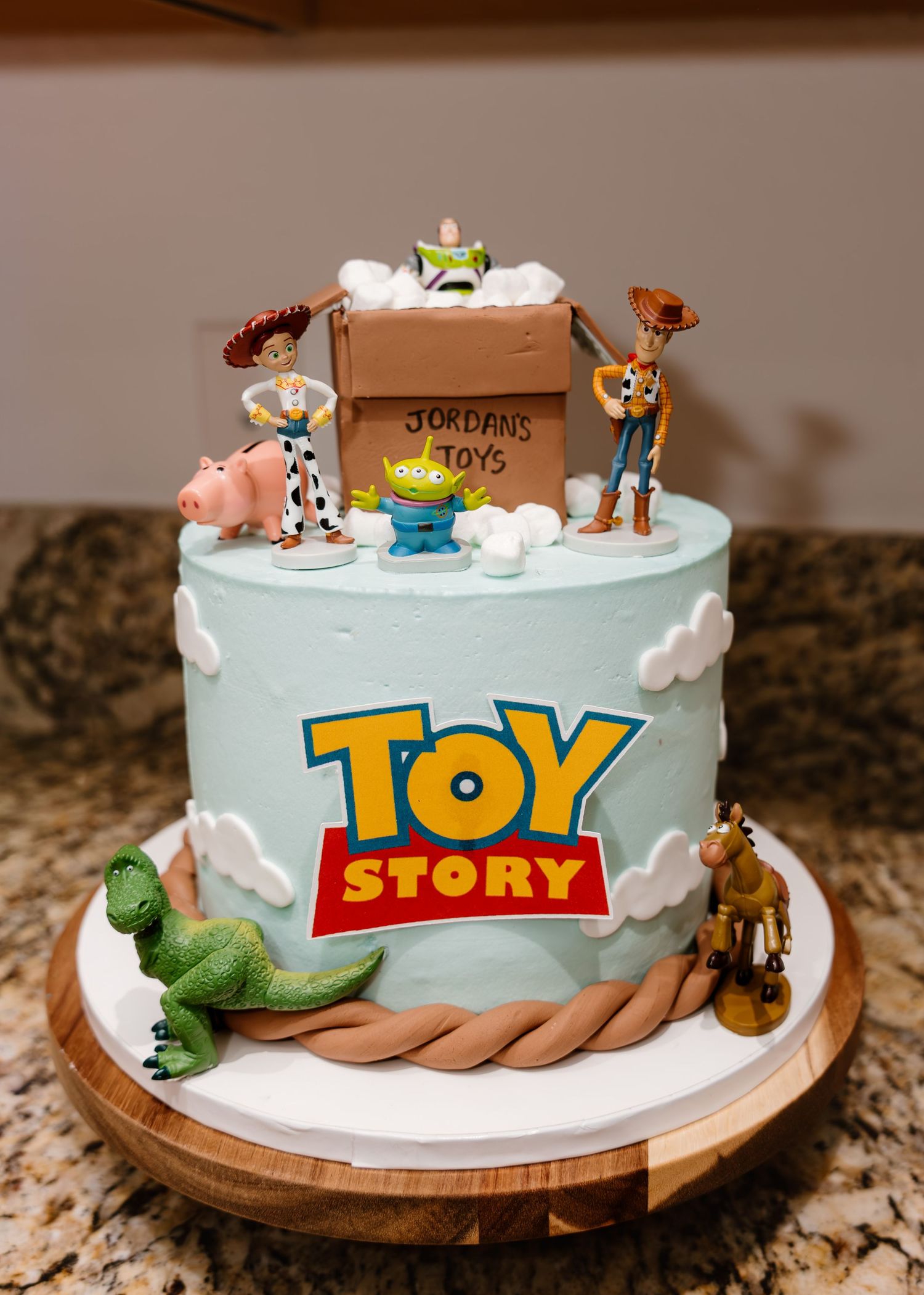 Toy Story themed birthday cake with Woody, Buzz, and friends on top, reading Jordan's Toys, on a wooden board.