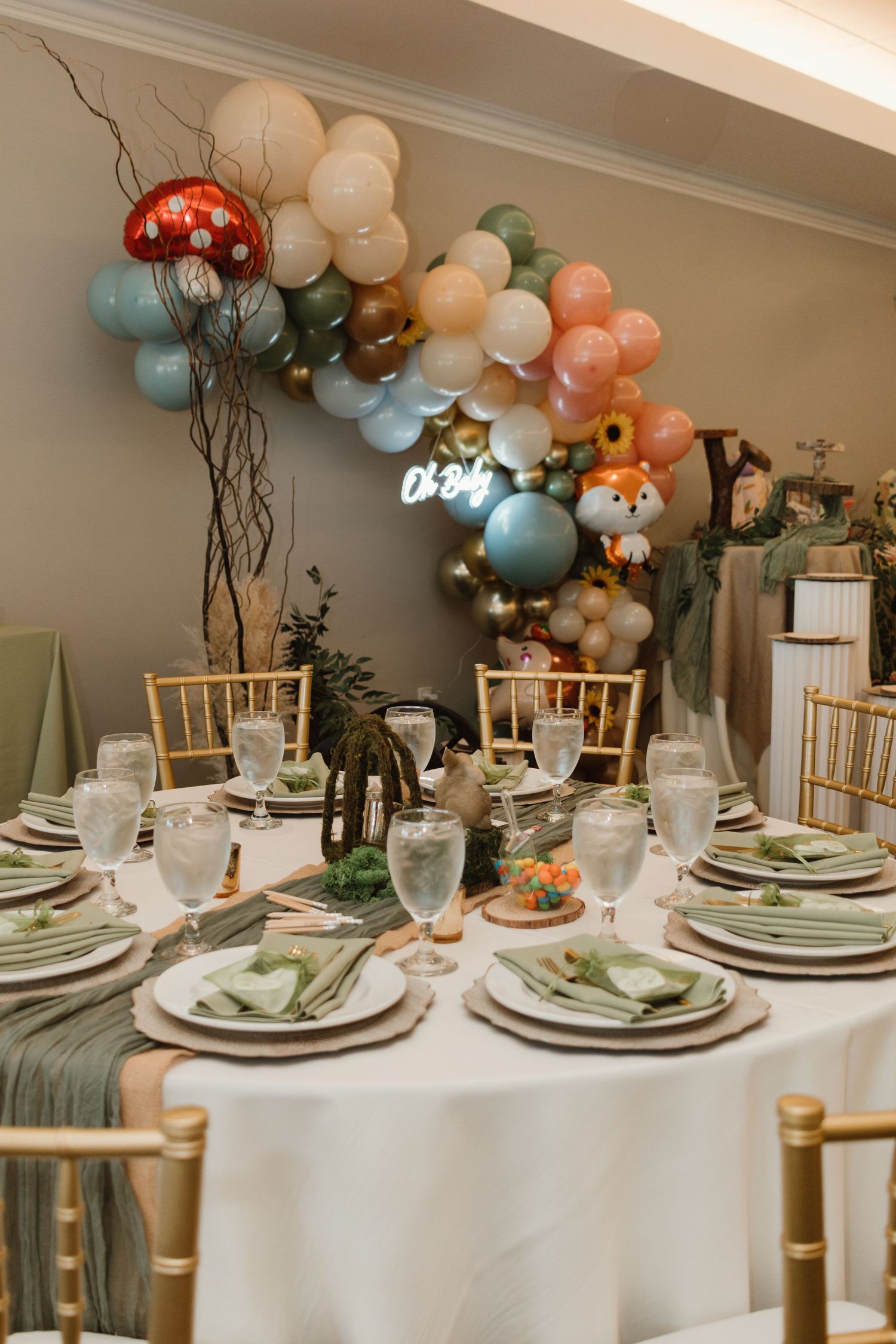 Elegant woodland baby shower table setting with green napkins and balloon arch backdrop.