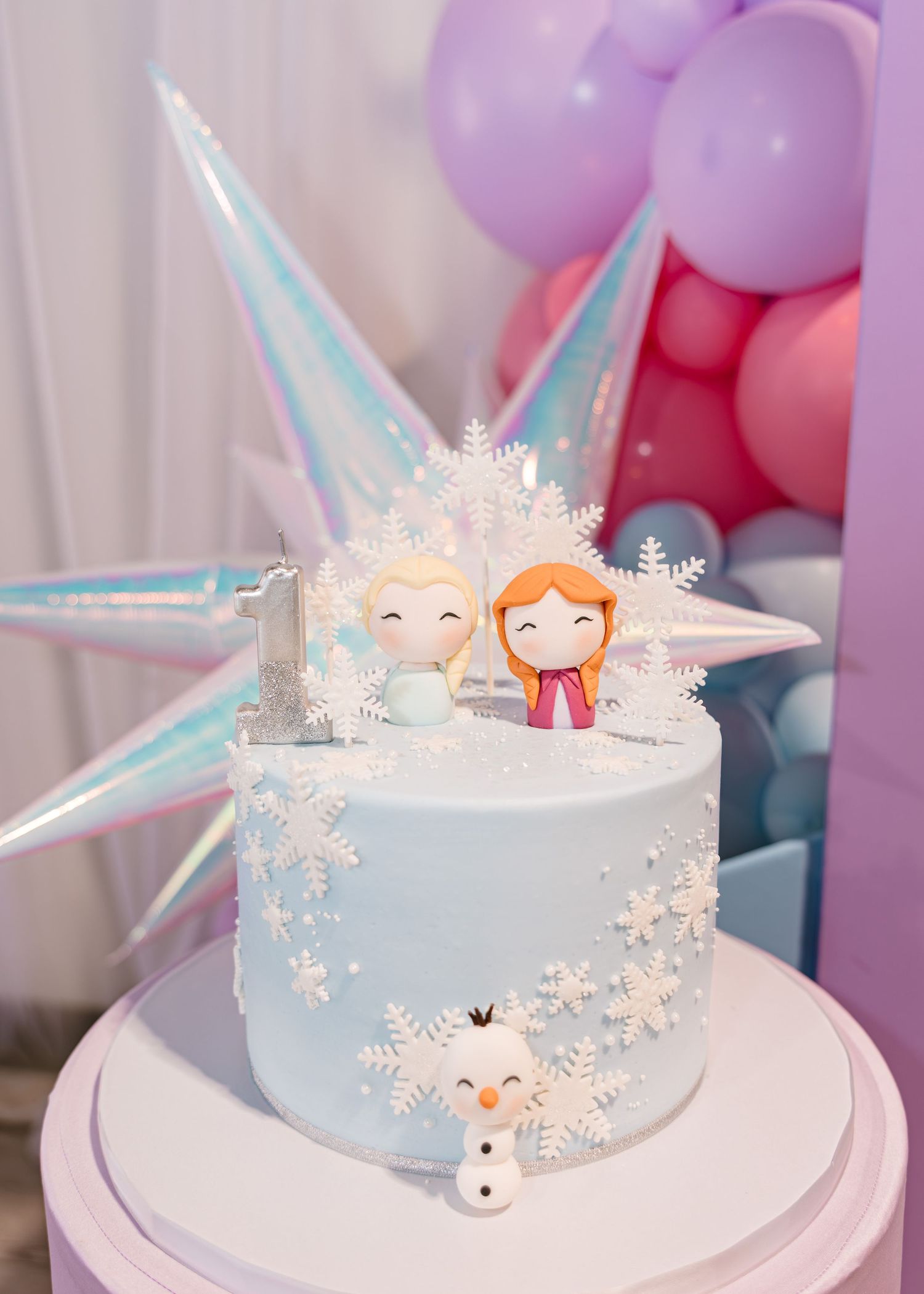 Light blue Frozen birthday cake with Elsa and Anna figurines, snowflakes, and Olaf decoration.