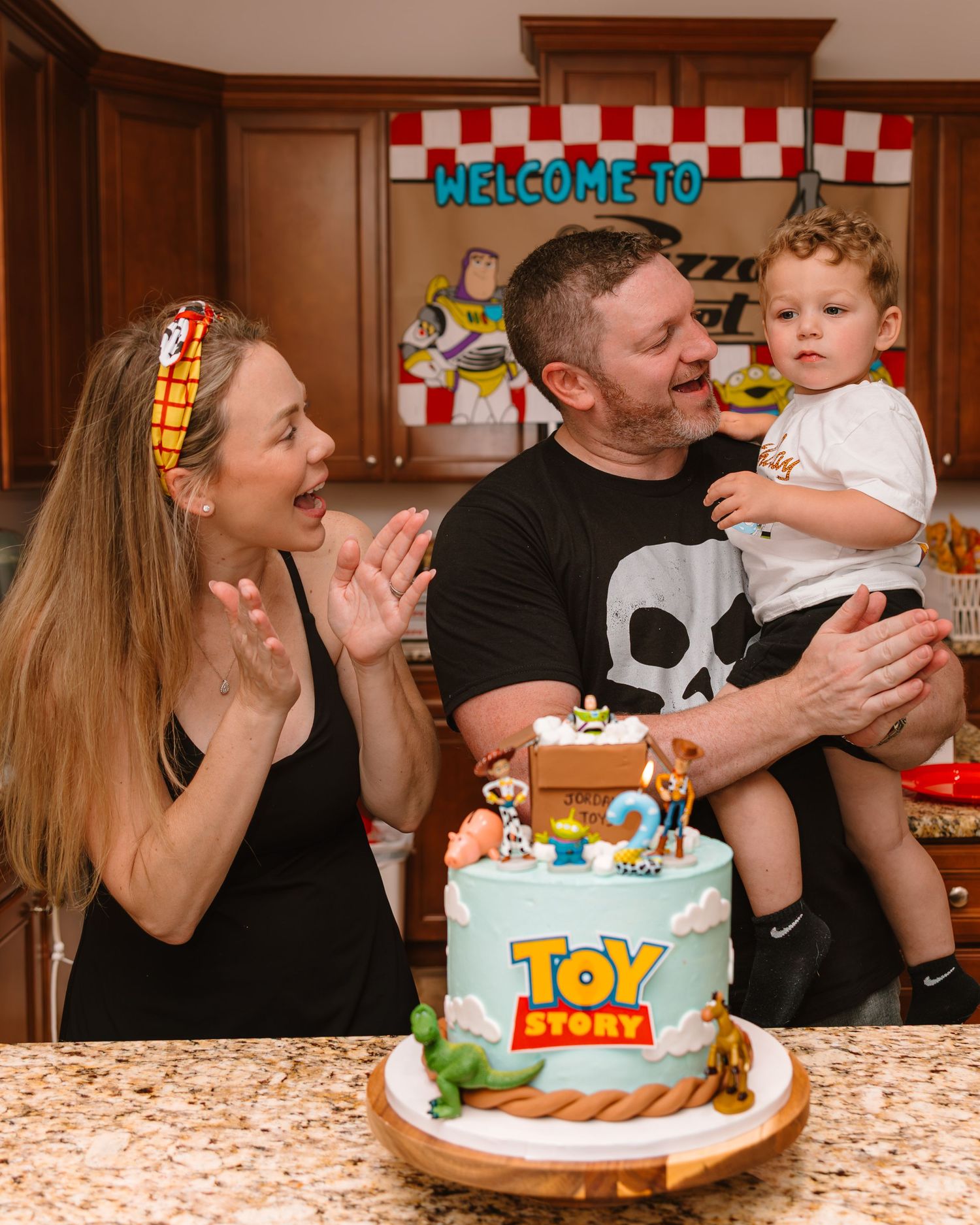 Family celebrates toddler's Toy Story birthday with themed cake featuring Woody and Buzz Lightyear decorations.