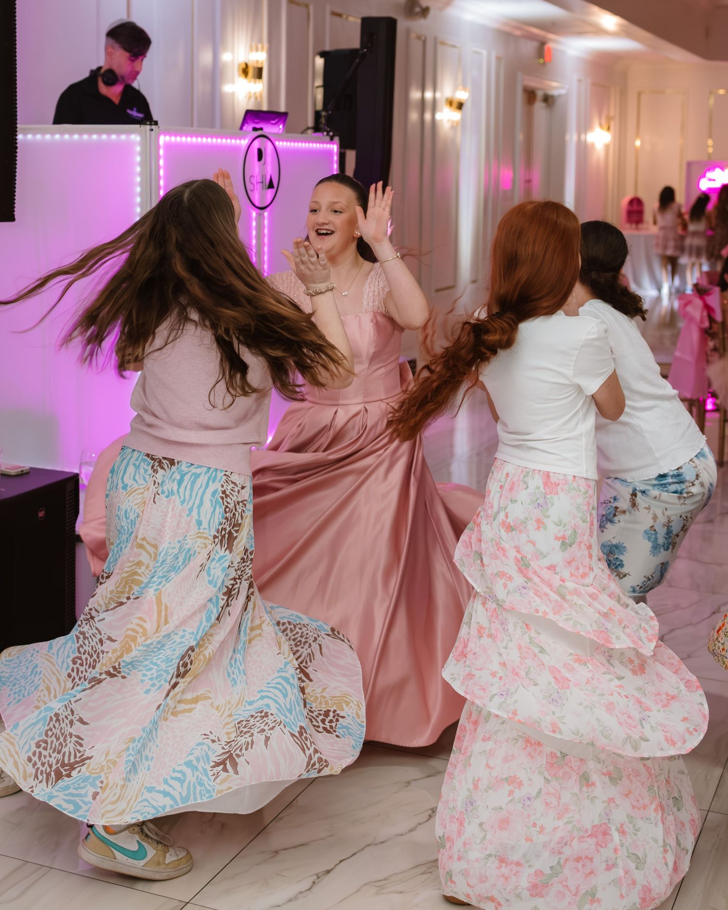 Girls dancing joyfully in floral skirts at a pink-themed birthday party celebration.