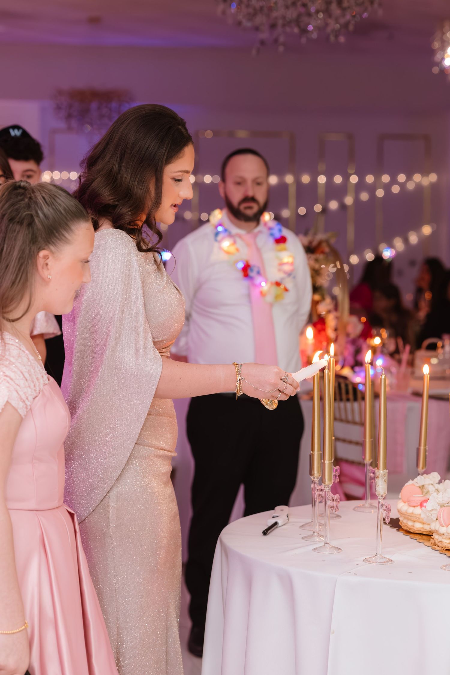 Elegant woman in pink gown lighting tall gold candles at a festive party celebration.