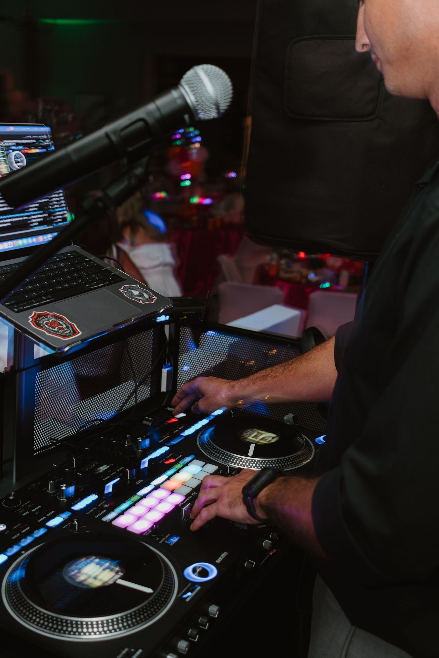 DJ operating professional turntables and mixer with laptop and microphone at a party event.