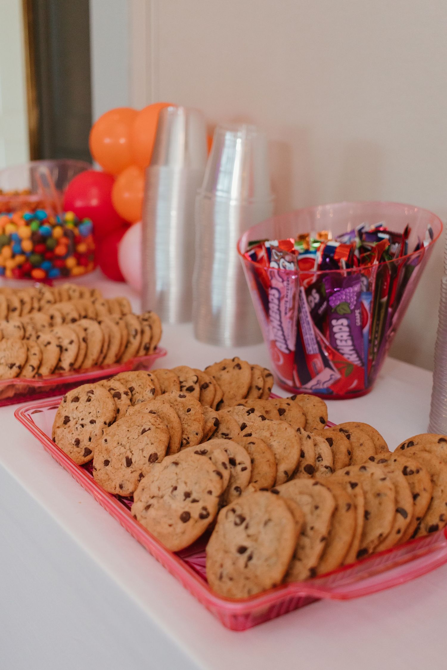 Sweet 16 party dessert table with chocolate chip cookies on pink trays and Sour Patch Kids candy in a pink bowl.