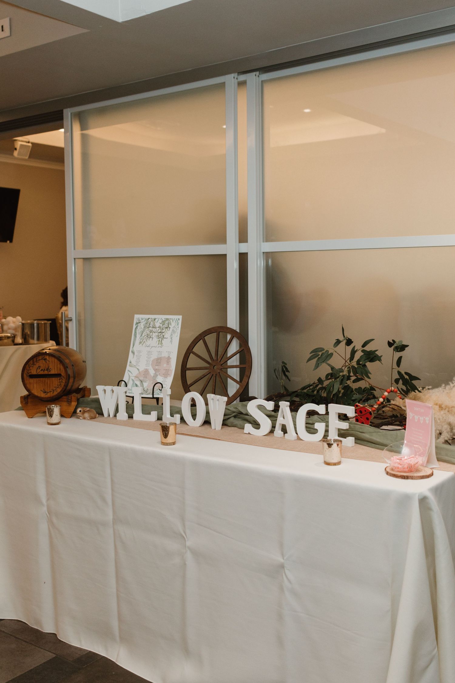 Baby shower gift table displaying large white letter signs spelling Willow Sage with rustic wooden wagon wheel decor.