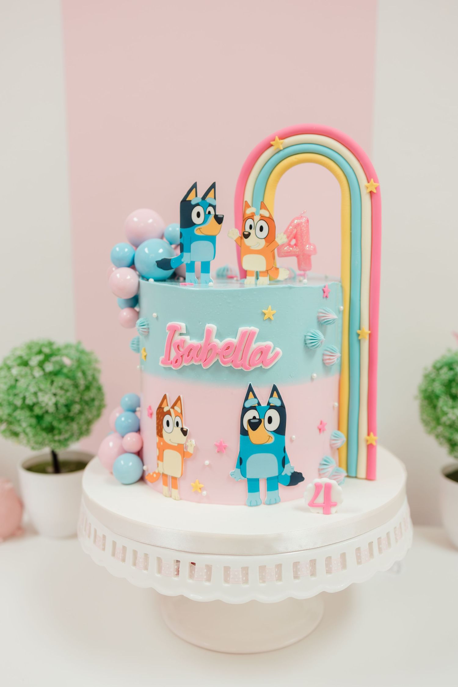 A blue Bluey-themed 4th birthday cake for Isabella with cartoon characters, rainbow, and pastel balloon decorations.