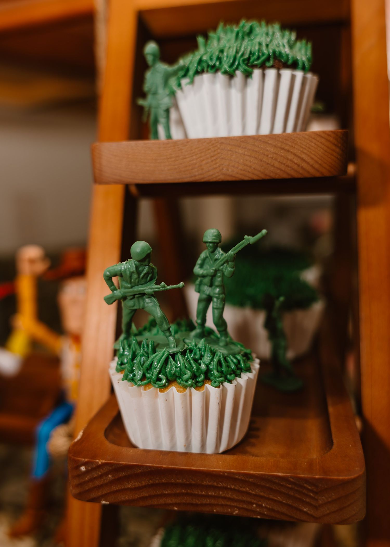 Green army soldier cupcake toppers on white frosted cupcakes displayed on a wooden tiered shelf.