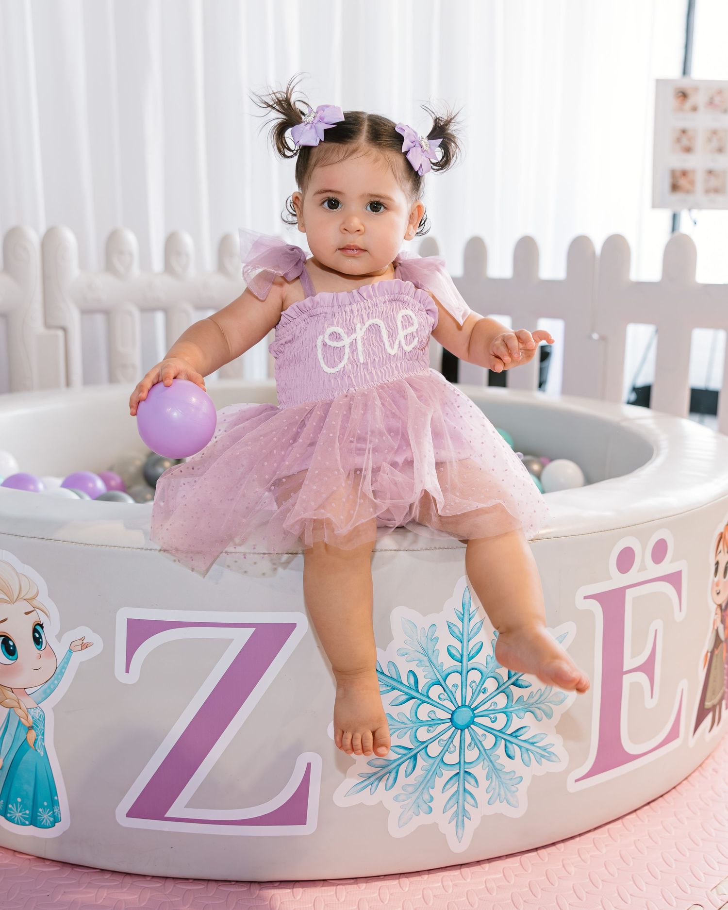 Baby girl in pink tutu sits on personalized Frozen-themed ball pit spelling ZOE.