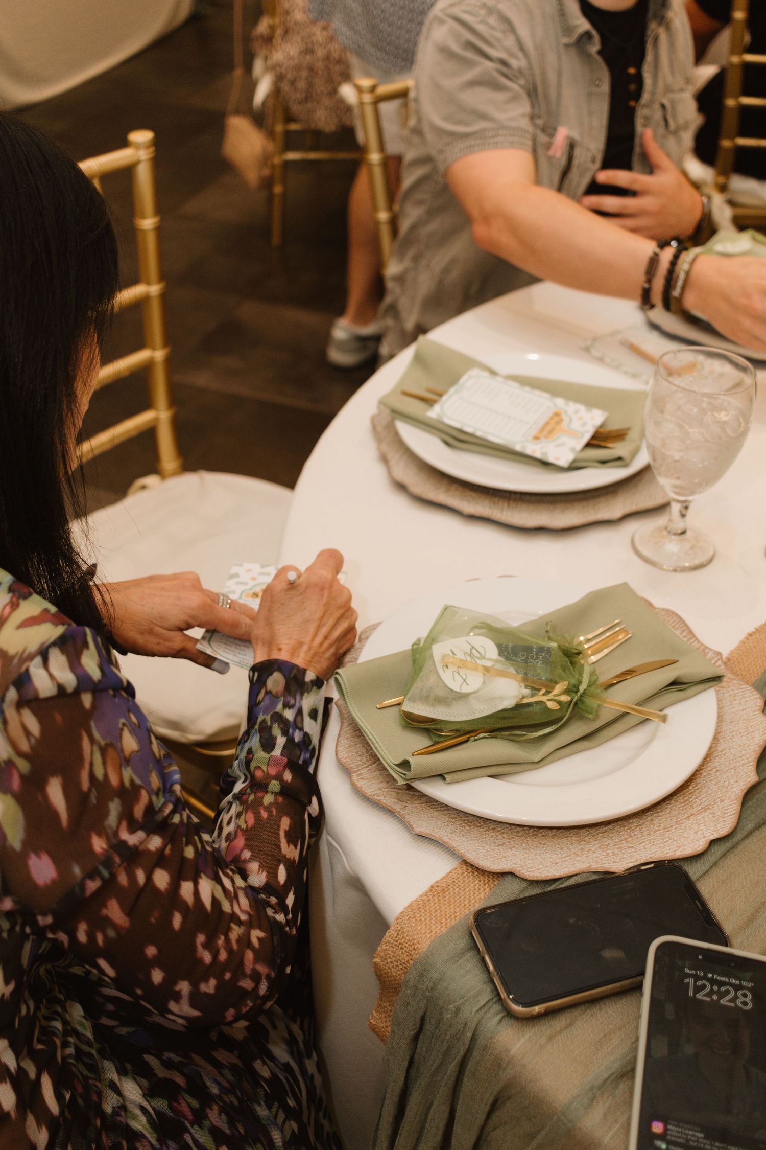 Guest writing on a card at an elegantly set round table with sage green napkins and gold cutlery.