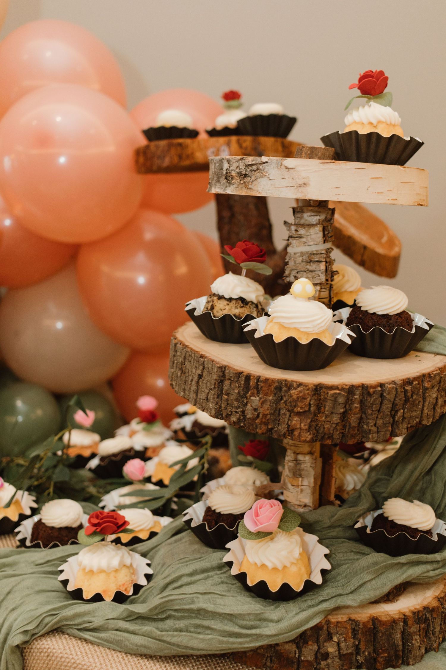 Rustic wooden tiered stand displaying chocolate cupcakes with white frosting and floral decorations at a party.