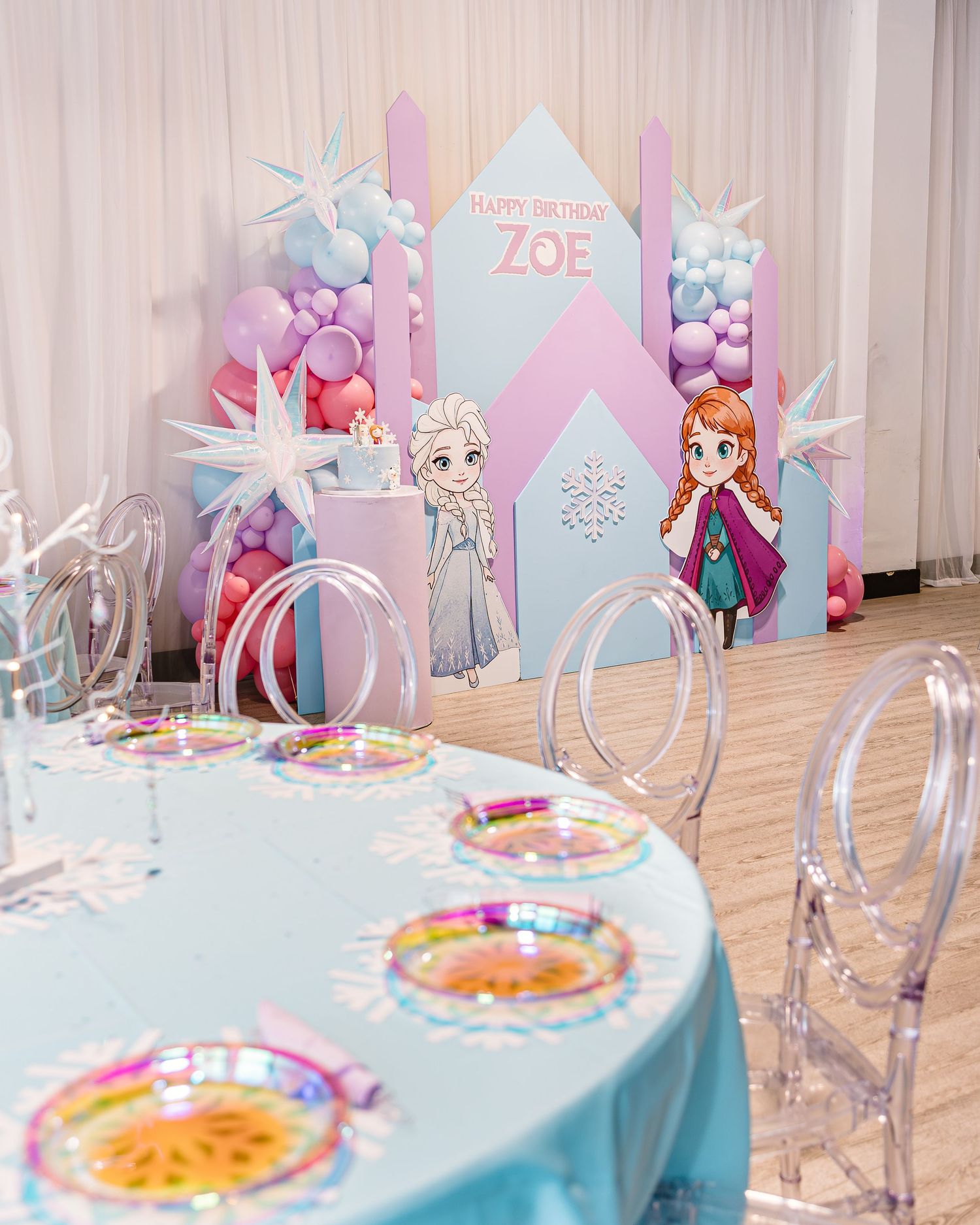 Frozen-themed first birthday party setup with Zoe backdrop, balloon arch, and decorated table.