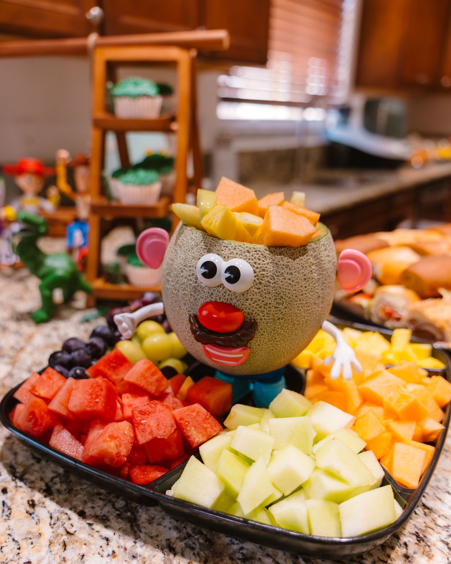 Mr. Potato Head fruit platter centerpiece surrounded by colorful melon, watermelon, and berry pieces.