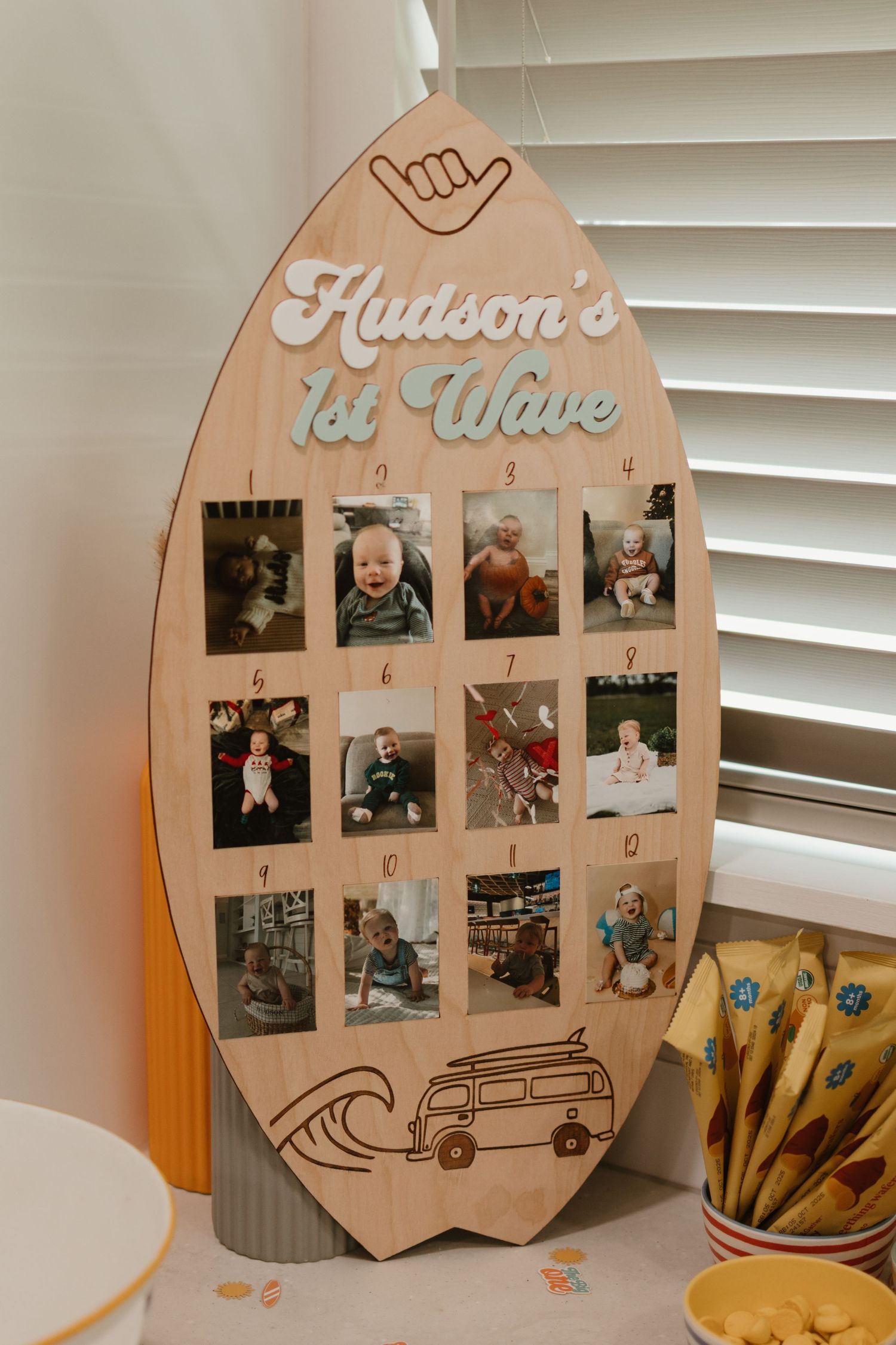 Wooden surfboard-shaped photo display showing Hudson's monthly milestone photos for first birthday.
