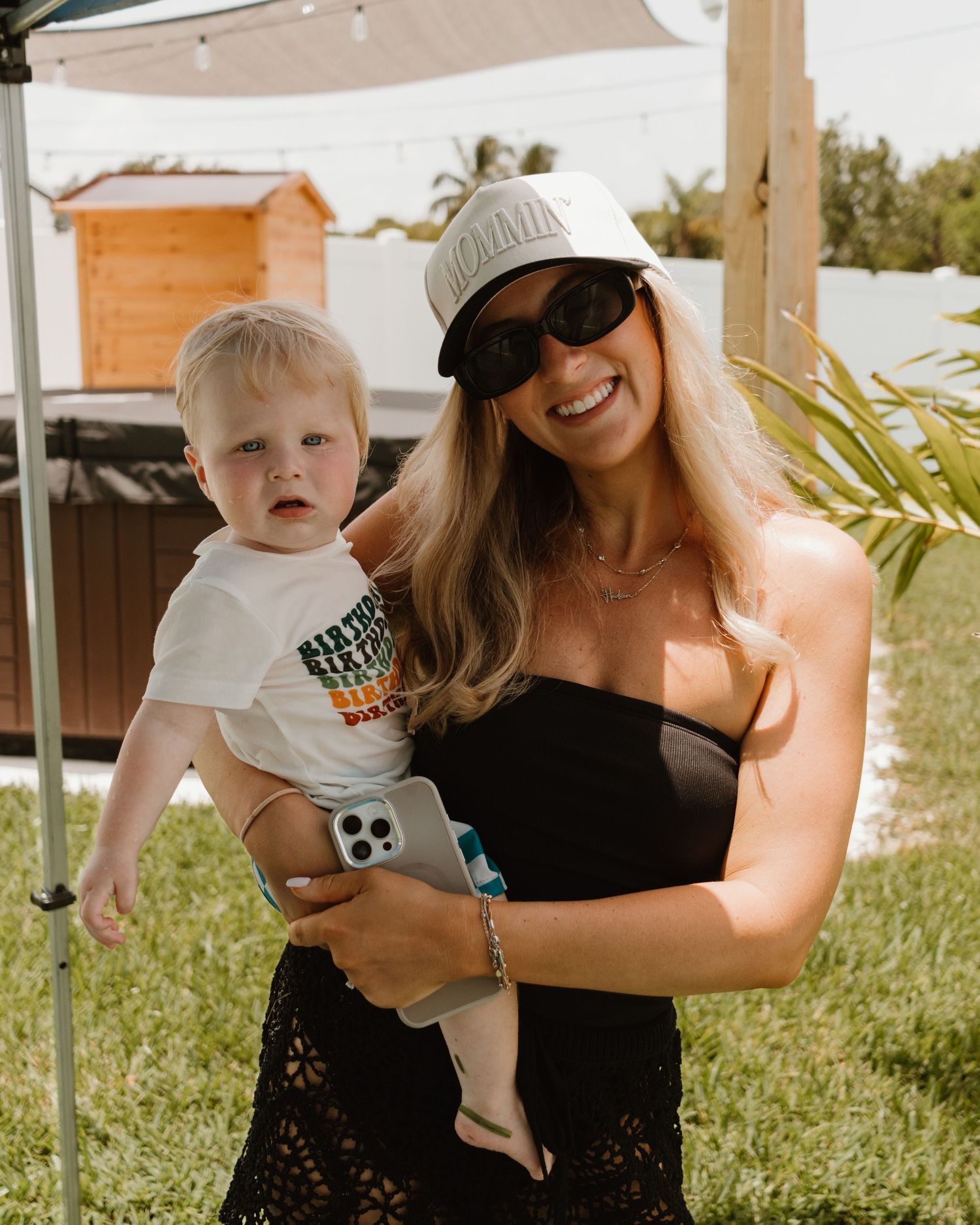 Smiling blonde mother holding her baby boy at an outdoor first birthday party.