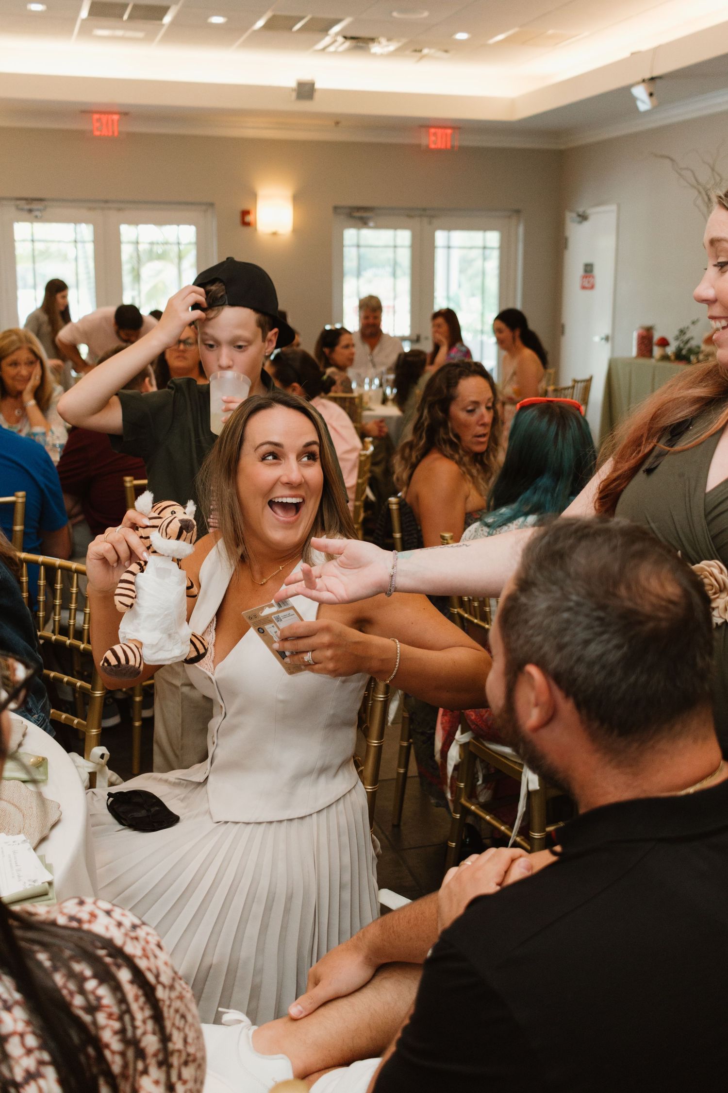 Excited woman holding a chocolate-dipped treat and laughing with guests at a lively baby shower celebration.