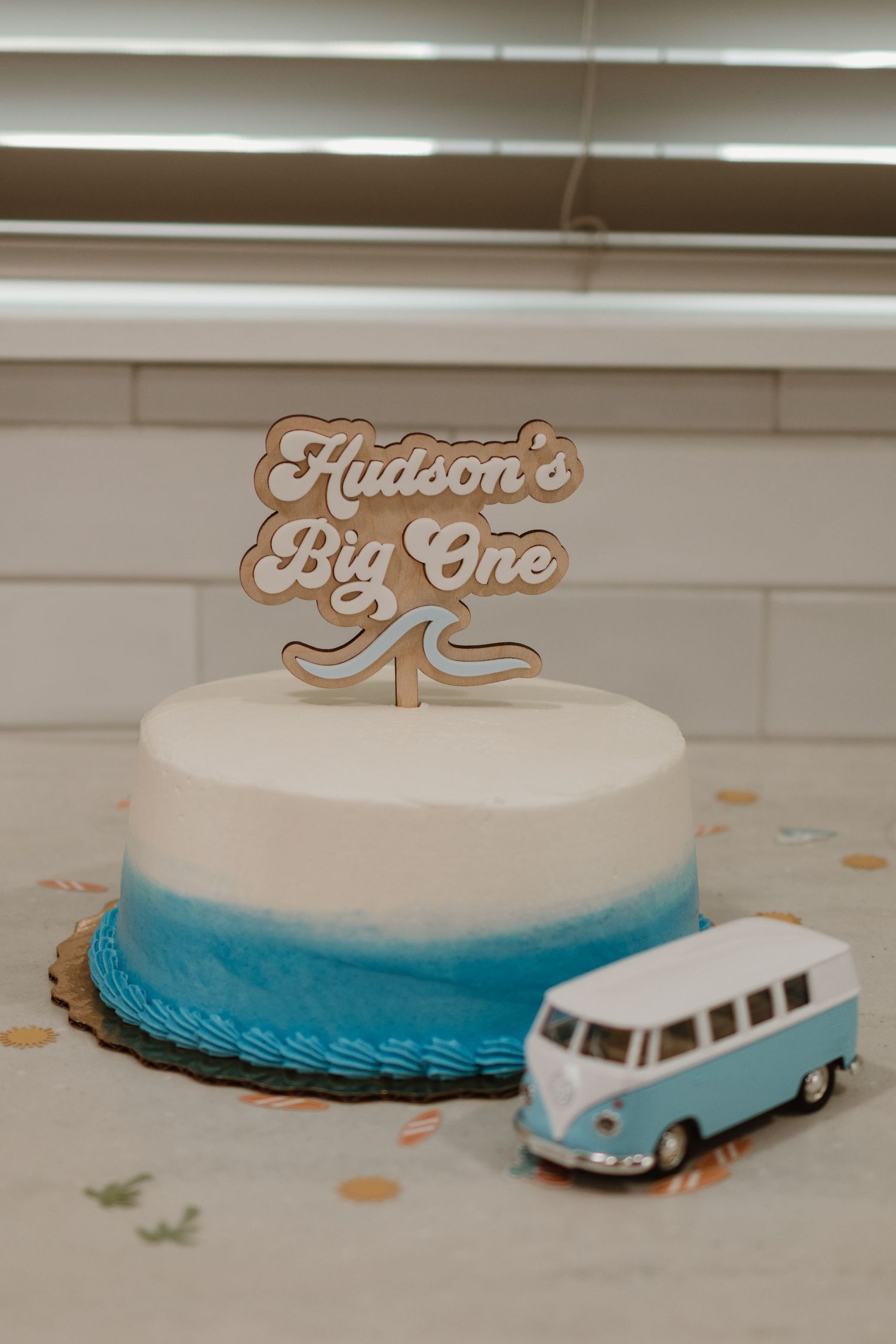 White and blue ombre first birthday cake with Hudson's Big One topper and toy VW bus.