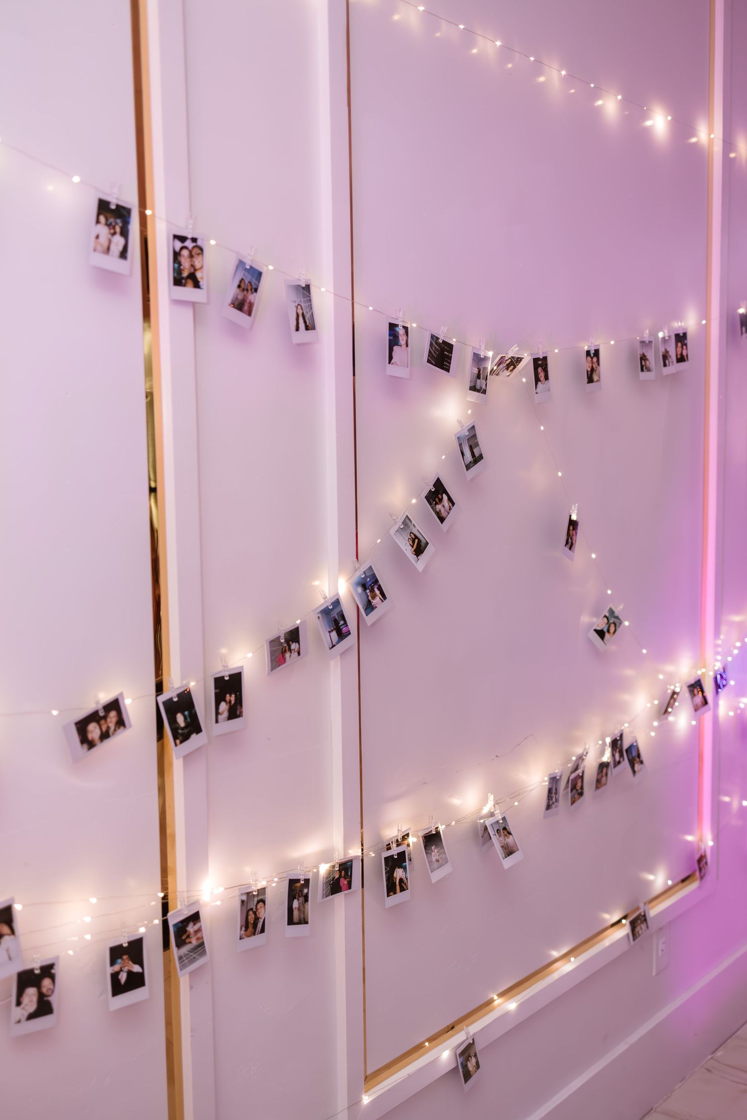 Decorative photo wall display with polaroid pictures and warm fairy string lights.