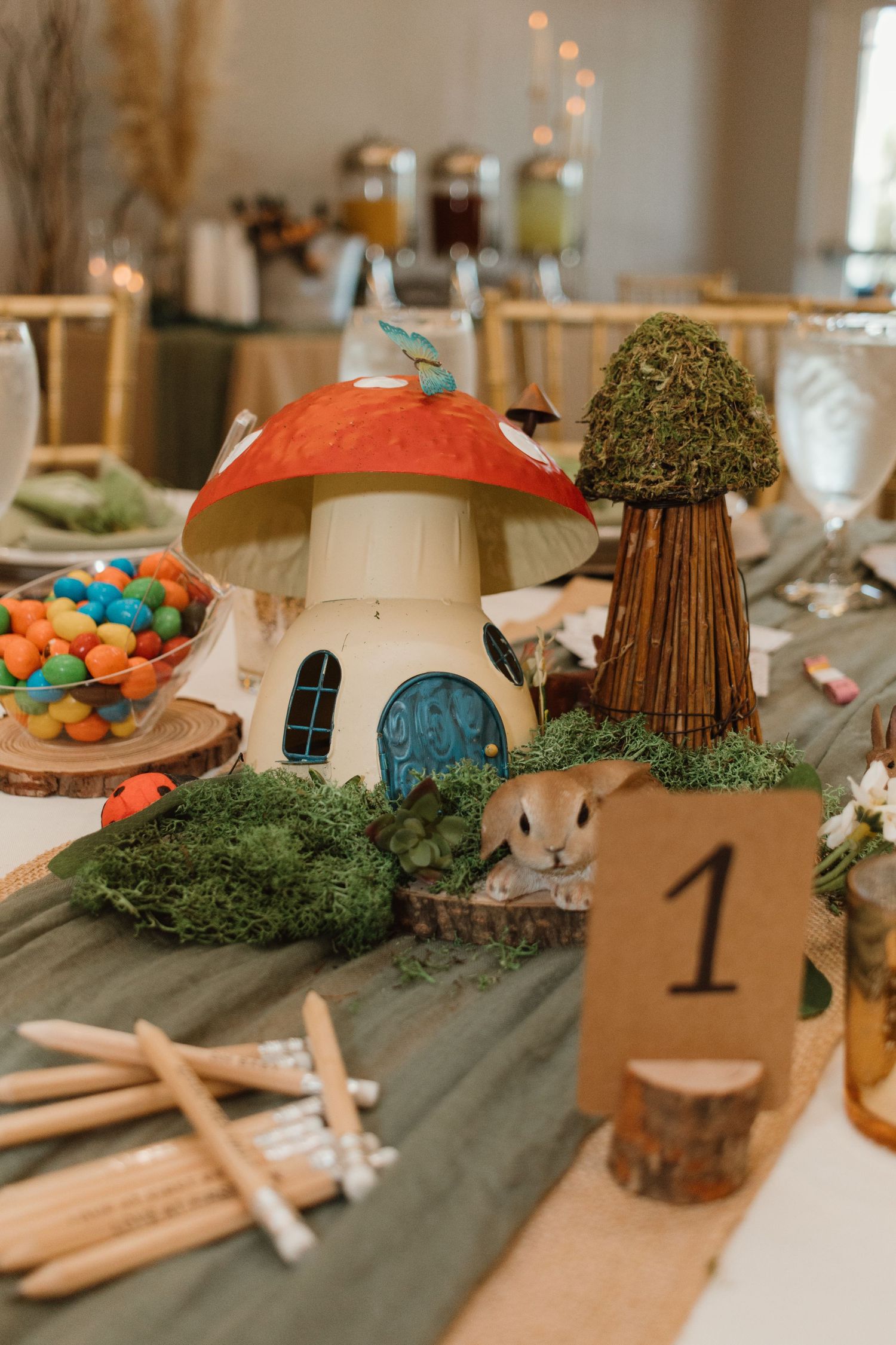 Enchanted forest baby shower centerpiece with mushroom house, moss, and woodland animals.