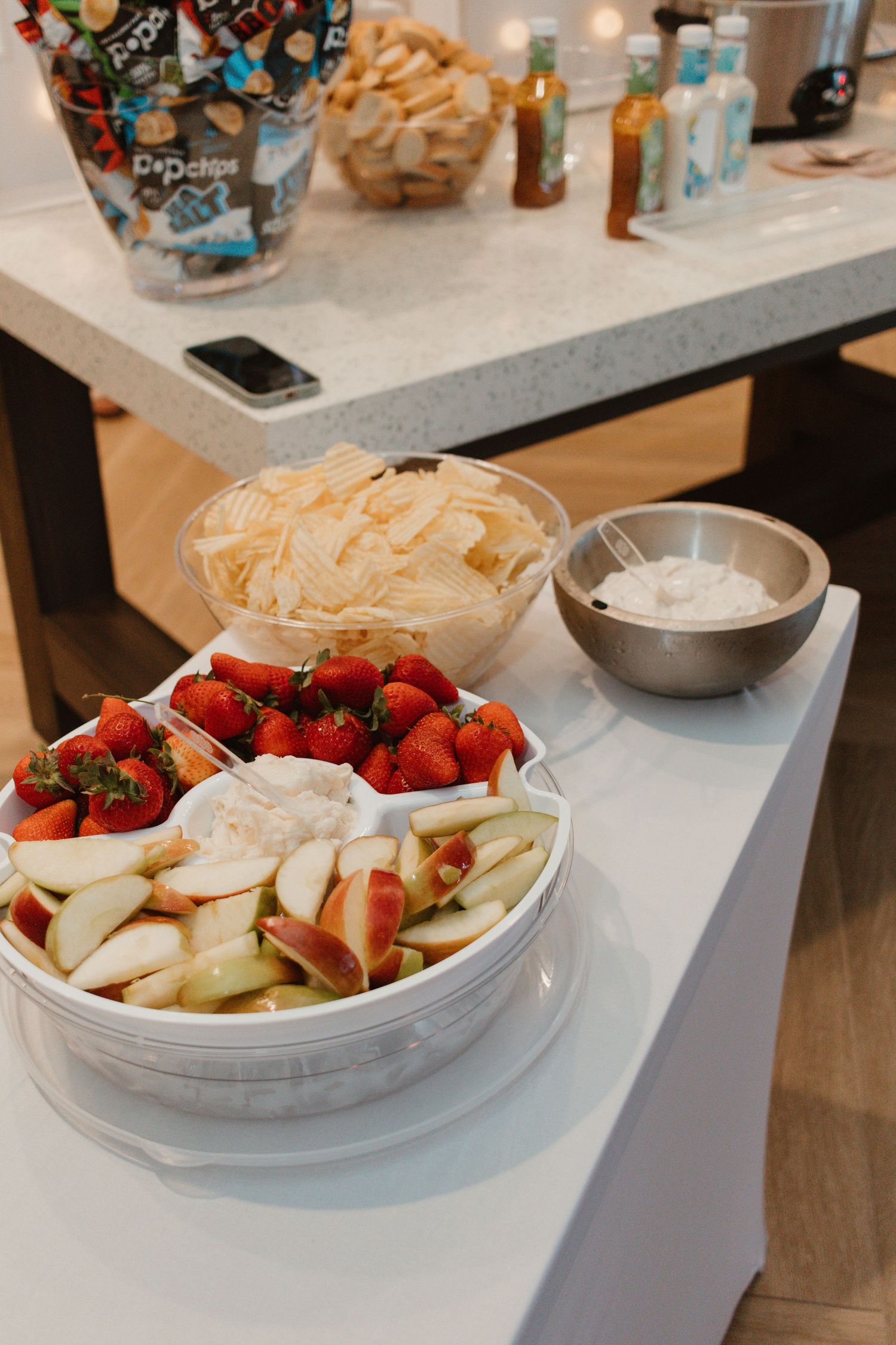 Party food table with a bowl of fresh strawberries, apple slices, white chocolate chips, and dipping sauce.