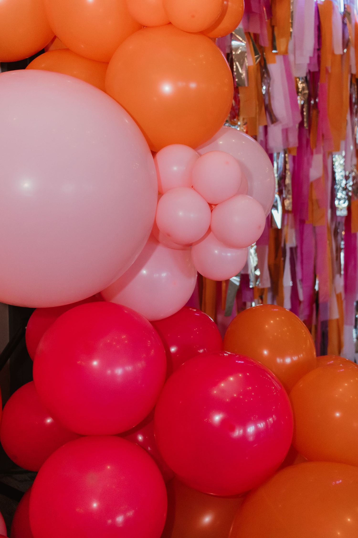 Colorful party balloon arrangement in pink, hot pink, and orange with streamer backdrop.