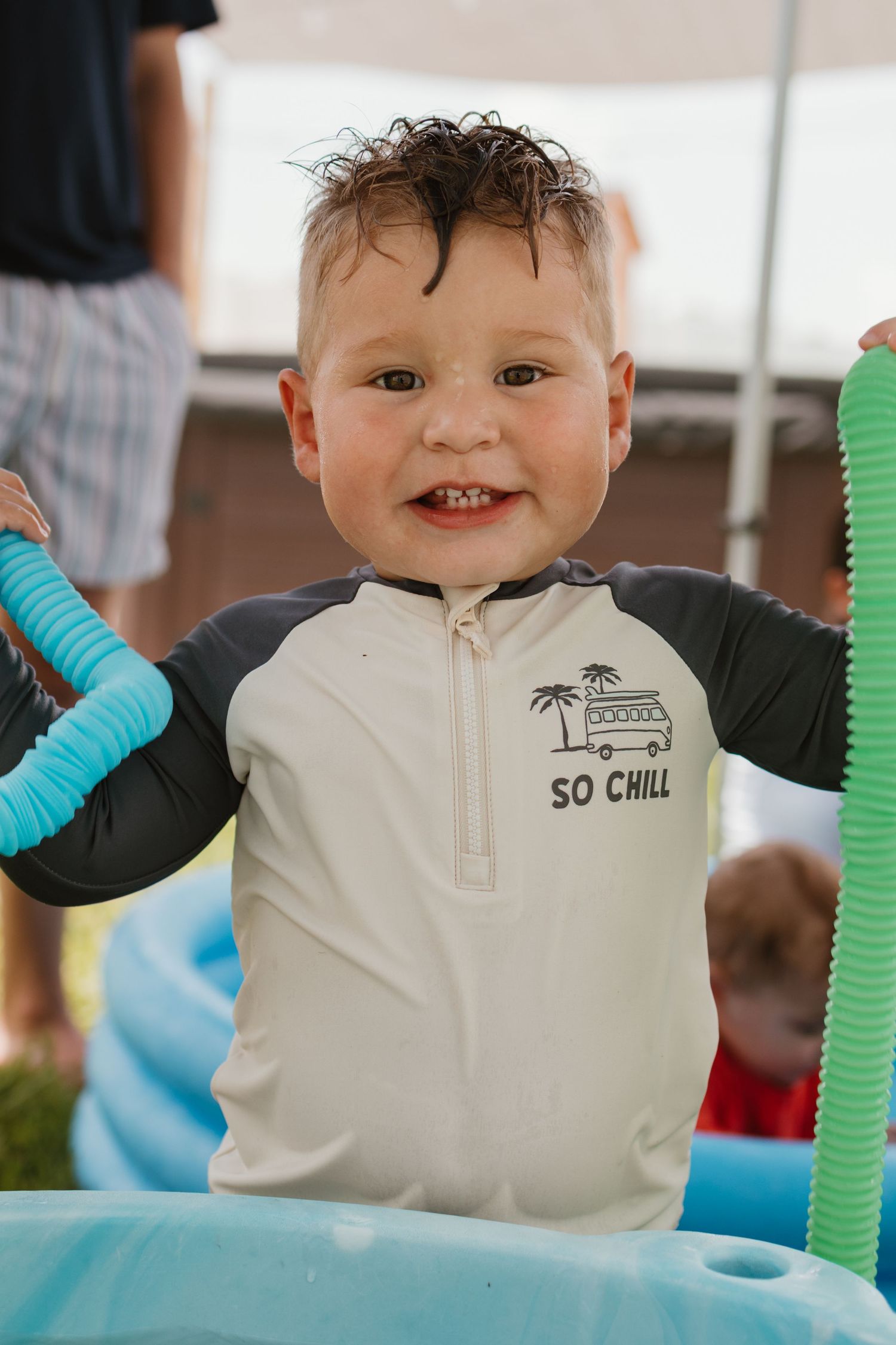 Smiling toddler boy in So Chill rashguard standing in inflatable pool at birthday party.