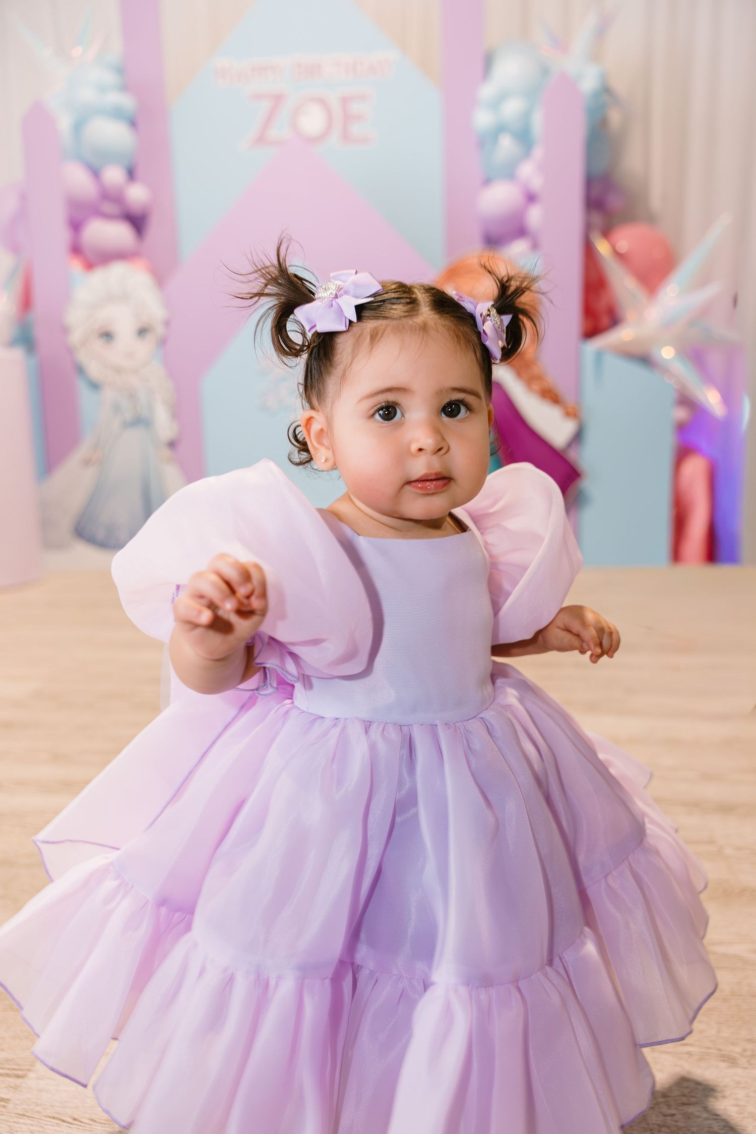 Baby girl in lavender tulle dress poses at her Frozen-themed first birthday party.