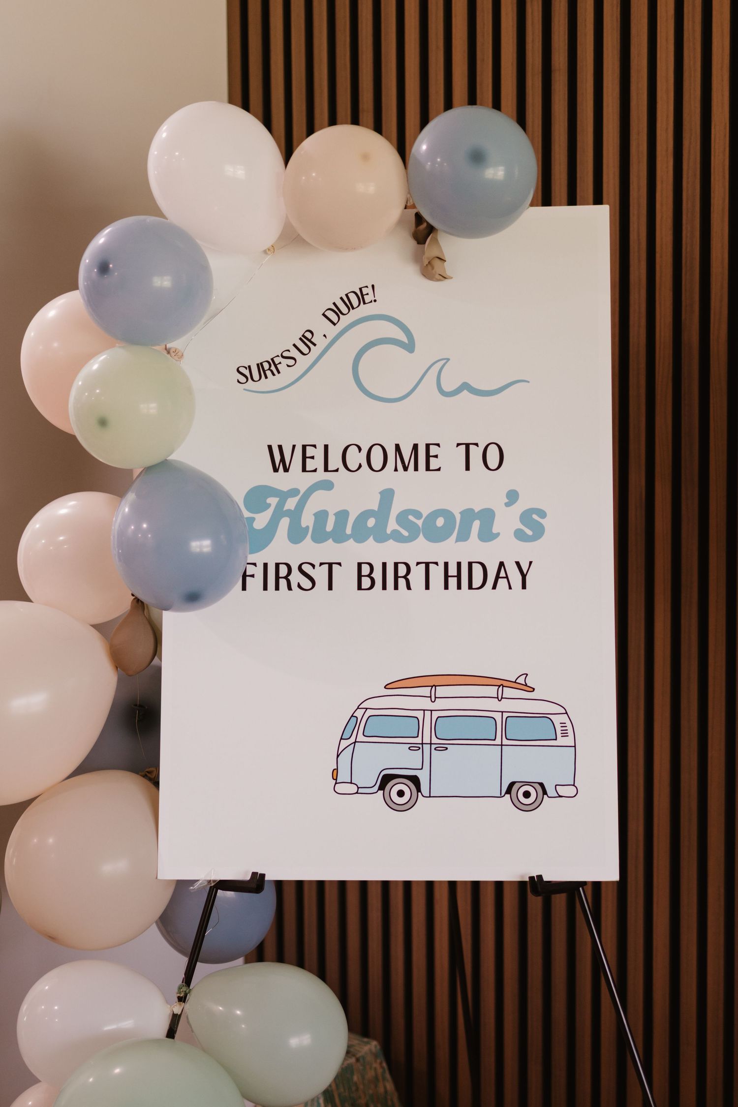 Welcome to Hudson First Birthday surf-themed party sign with blue and white balloon arch.