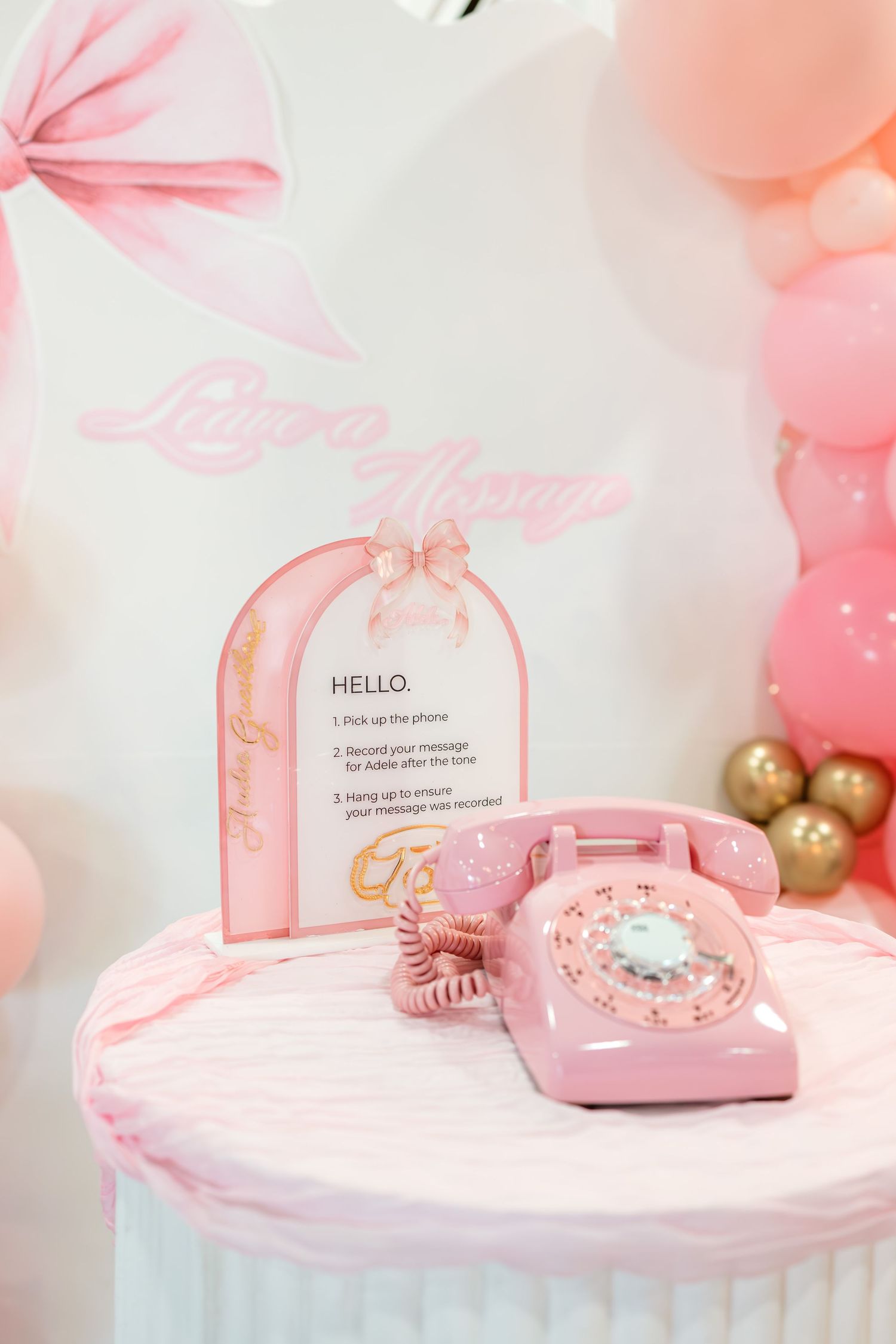 Pink vintage rotary phone leave-a-message station with balloon arch backdrop at birthday party.