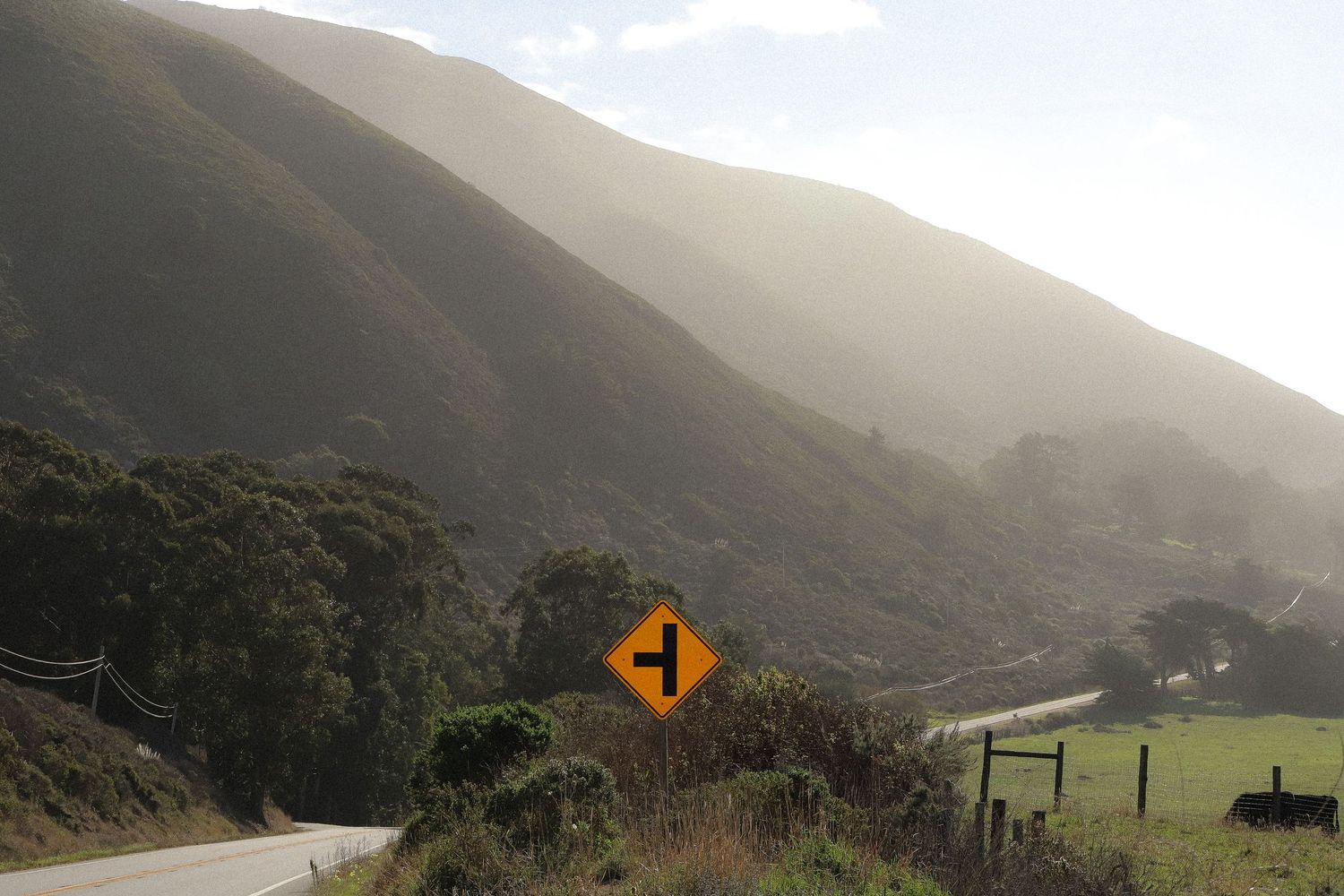 Scenic mountain road winding through green hills with fog rolling in.