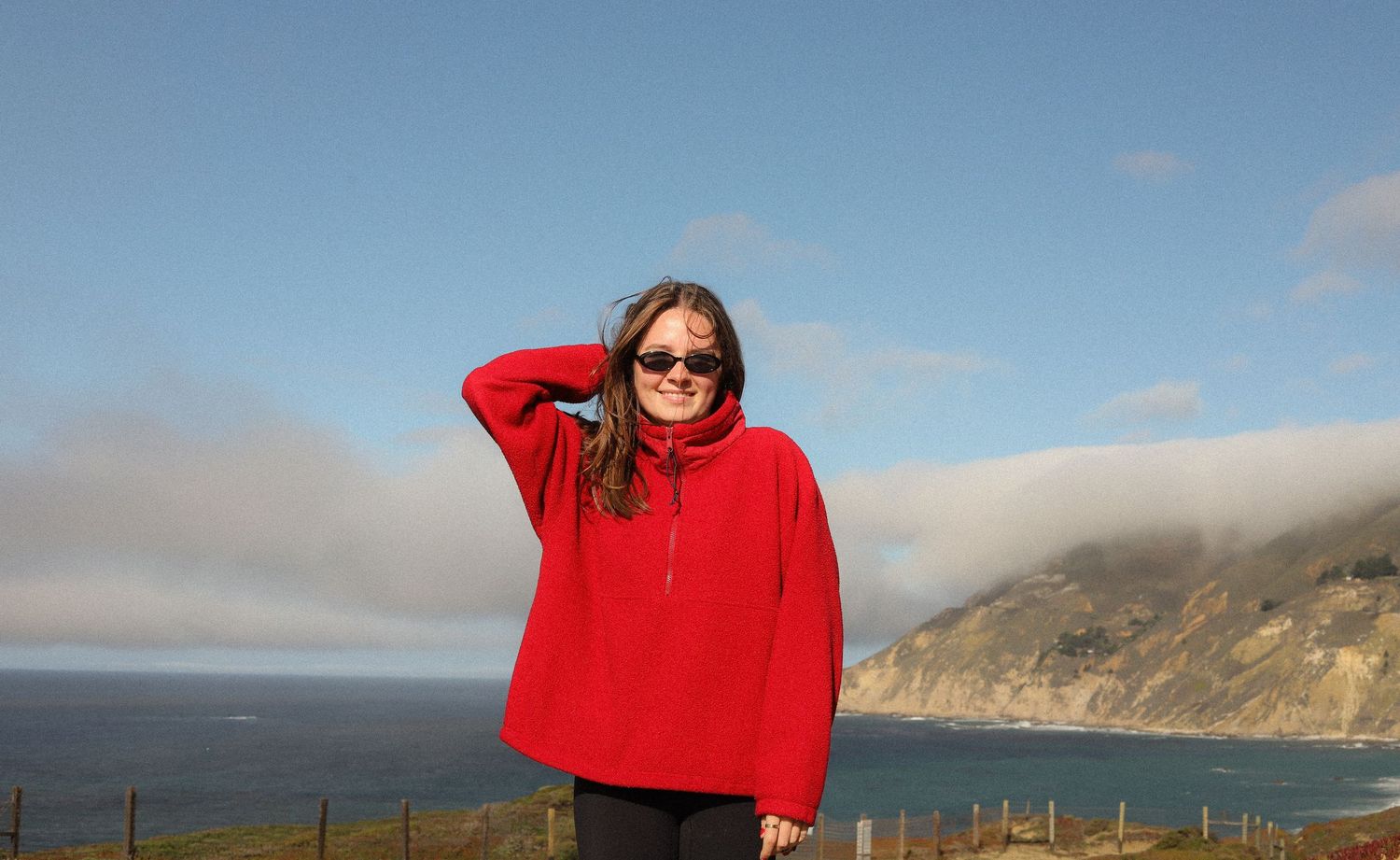 A panoramic sequence of coastal landscapes with a person in a bright red sweater against blue skies and cliffs.
