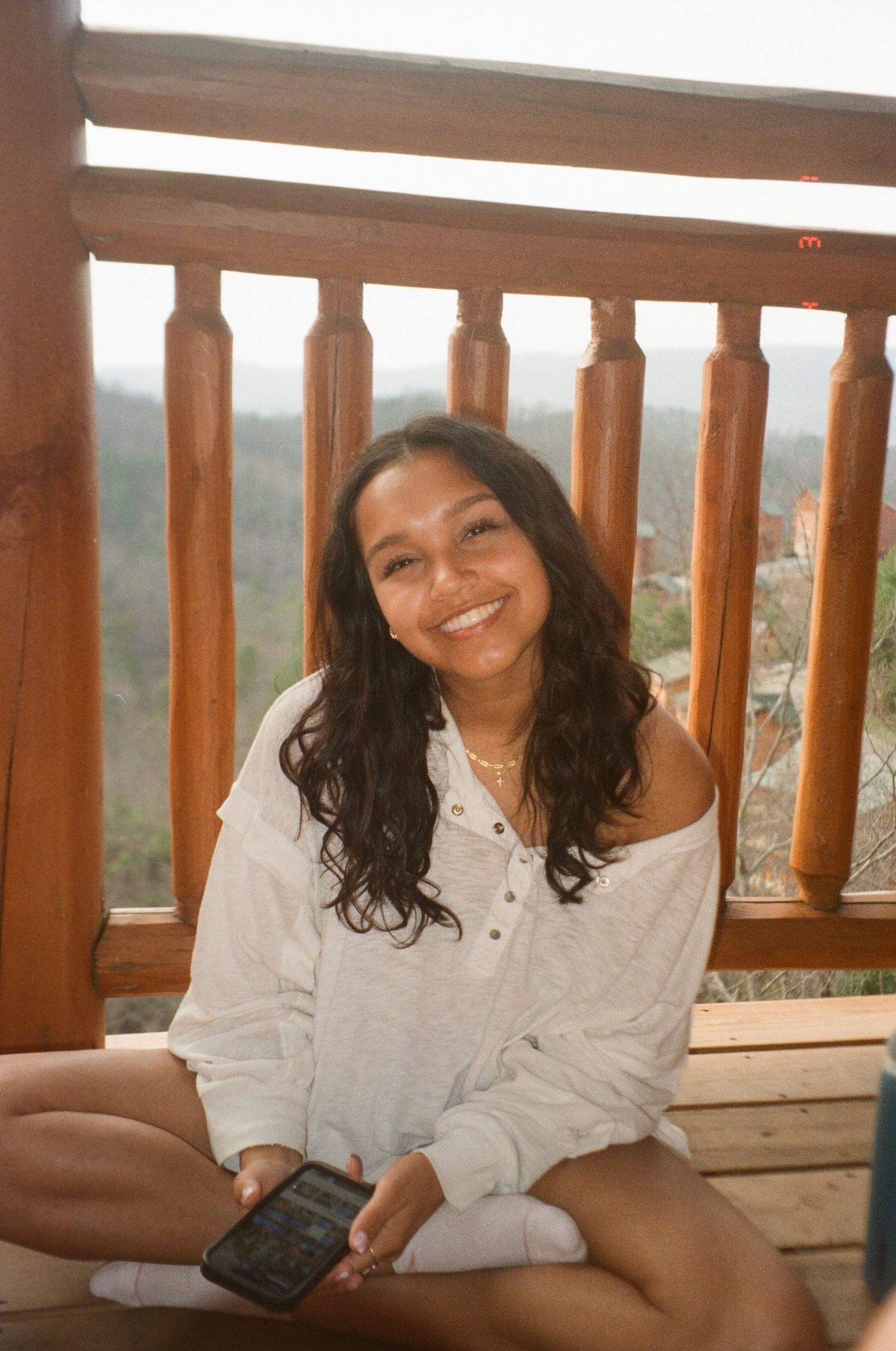 Person in white shirt relaxing on wooden deck railing with scenic mountain view in background.
