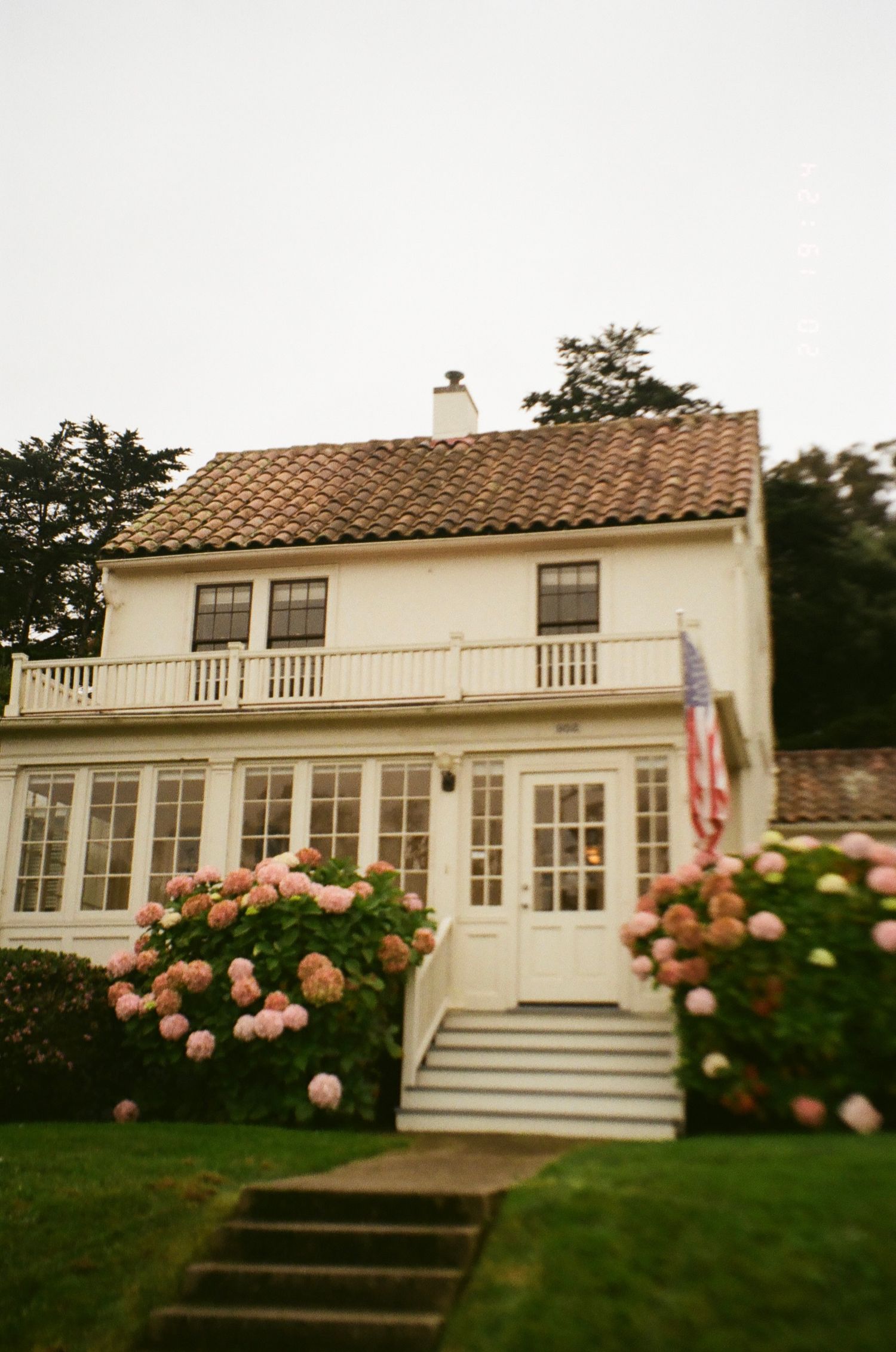 White coastal house with terracotta roof and pink roses blooming in the garden features classic colonial architecture.