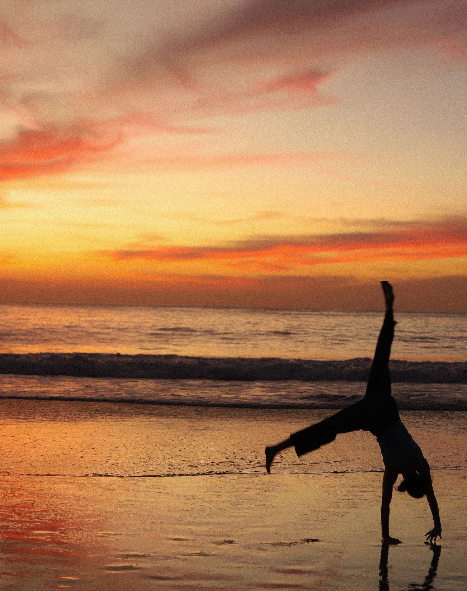 A sequence of silhouettes performing cartwheels and handstands on a beach at sunset with vibrant orange sky.