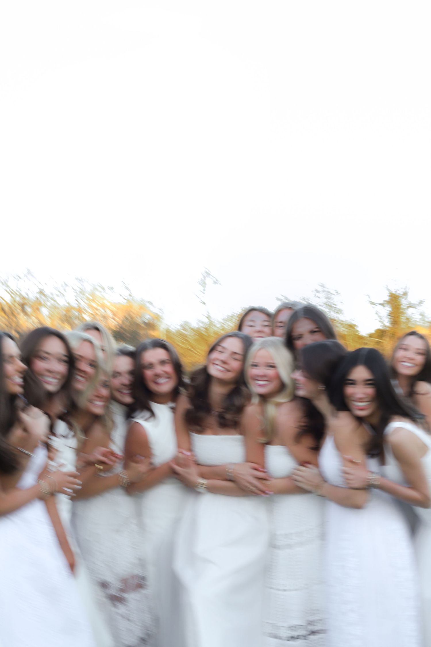 Joyful group photo of women in white dresses laughing together outdoors.