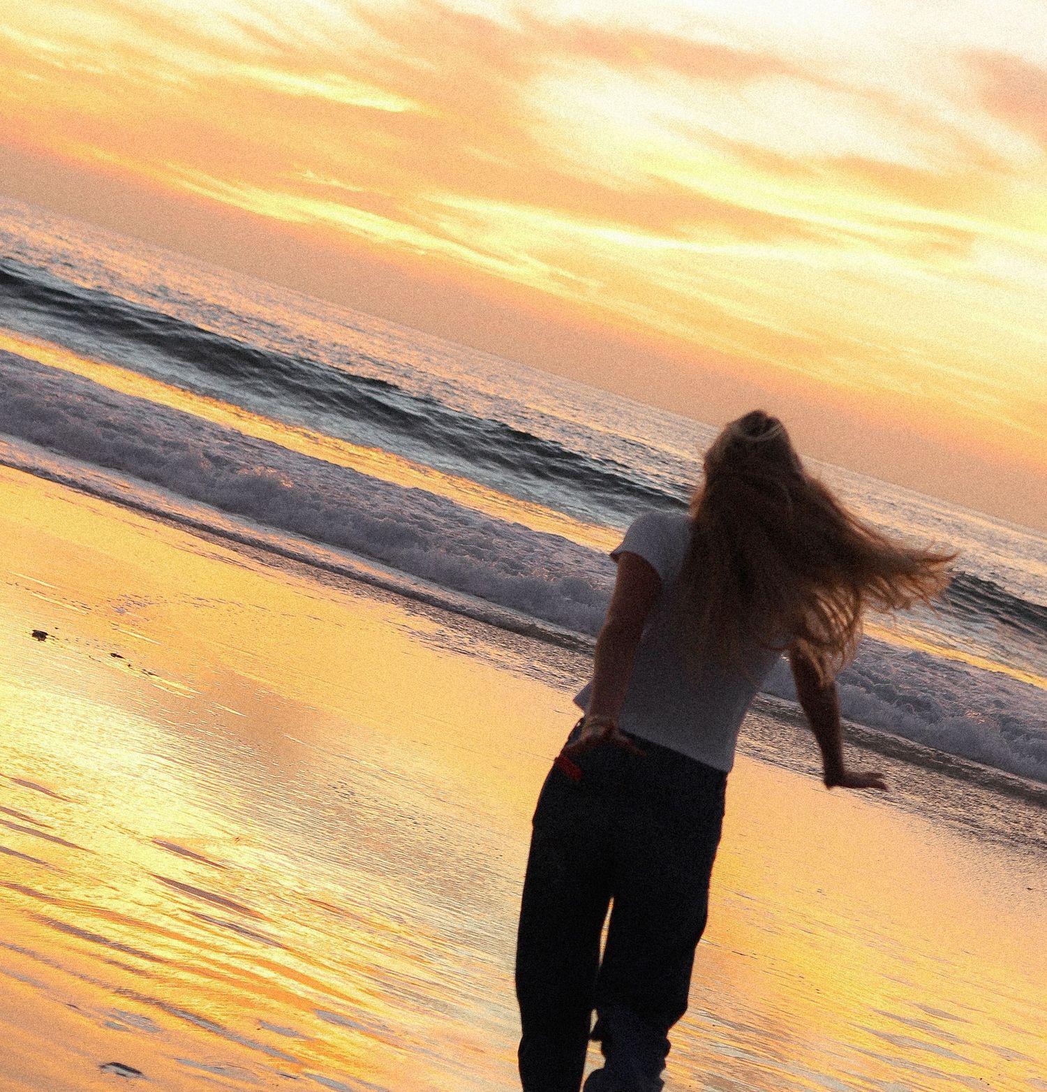 Silhouette of a figure dancing on a beach during a vibrant orange and golden sunset over the ocean.