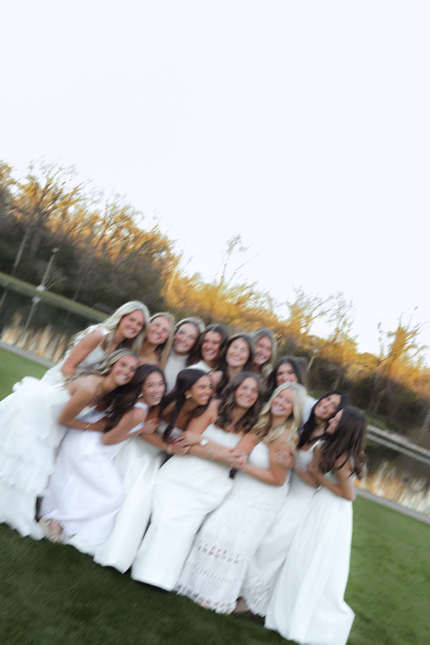 Group portrait series showing women in white dresses posing together on grass at sunset.