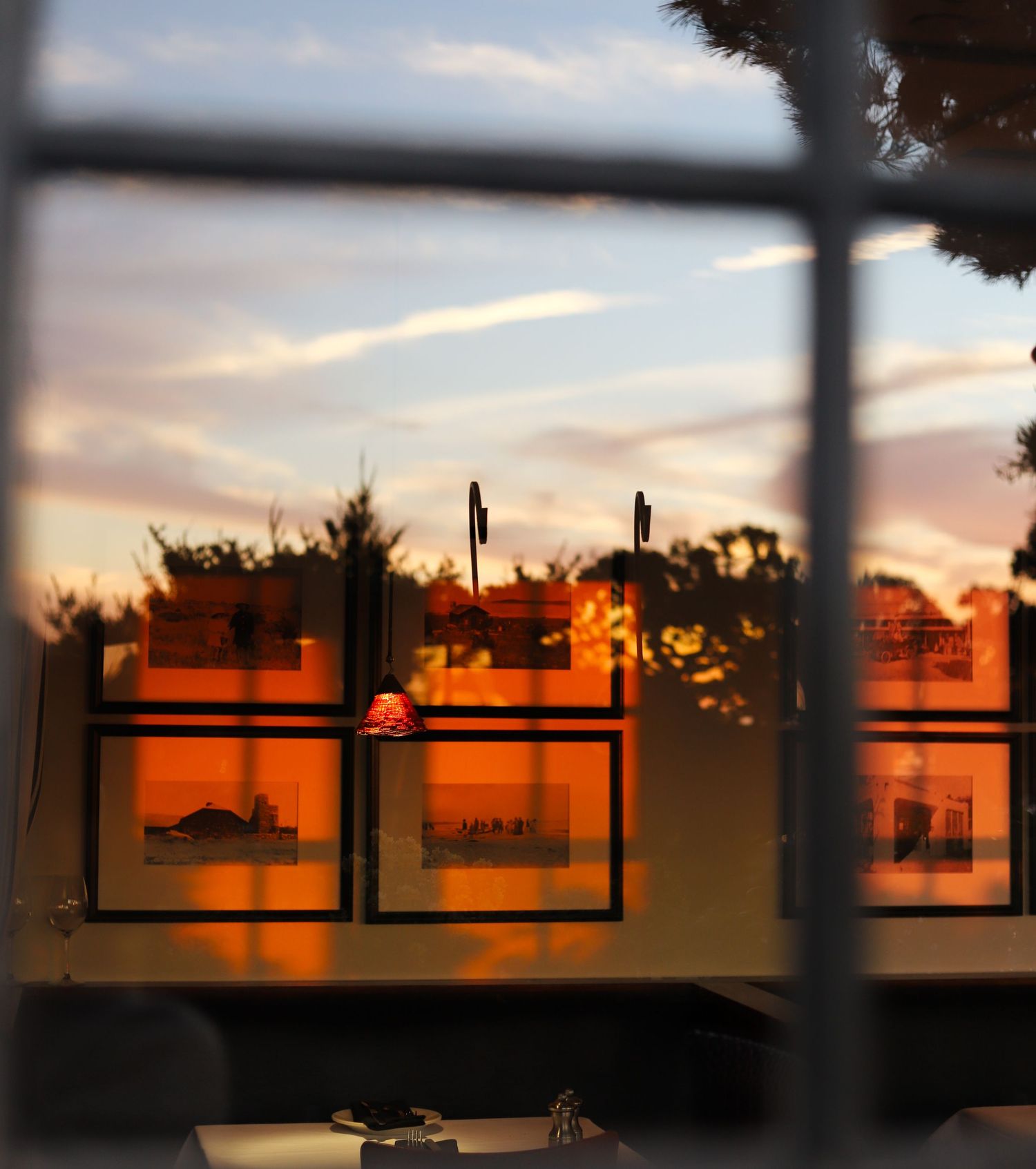 Sunset view through a window showing silhouetted buildings and trees against an orange and pink sky.