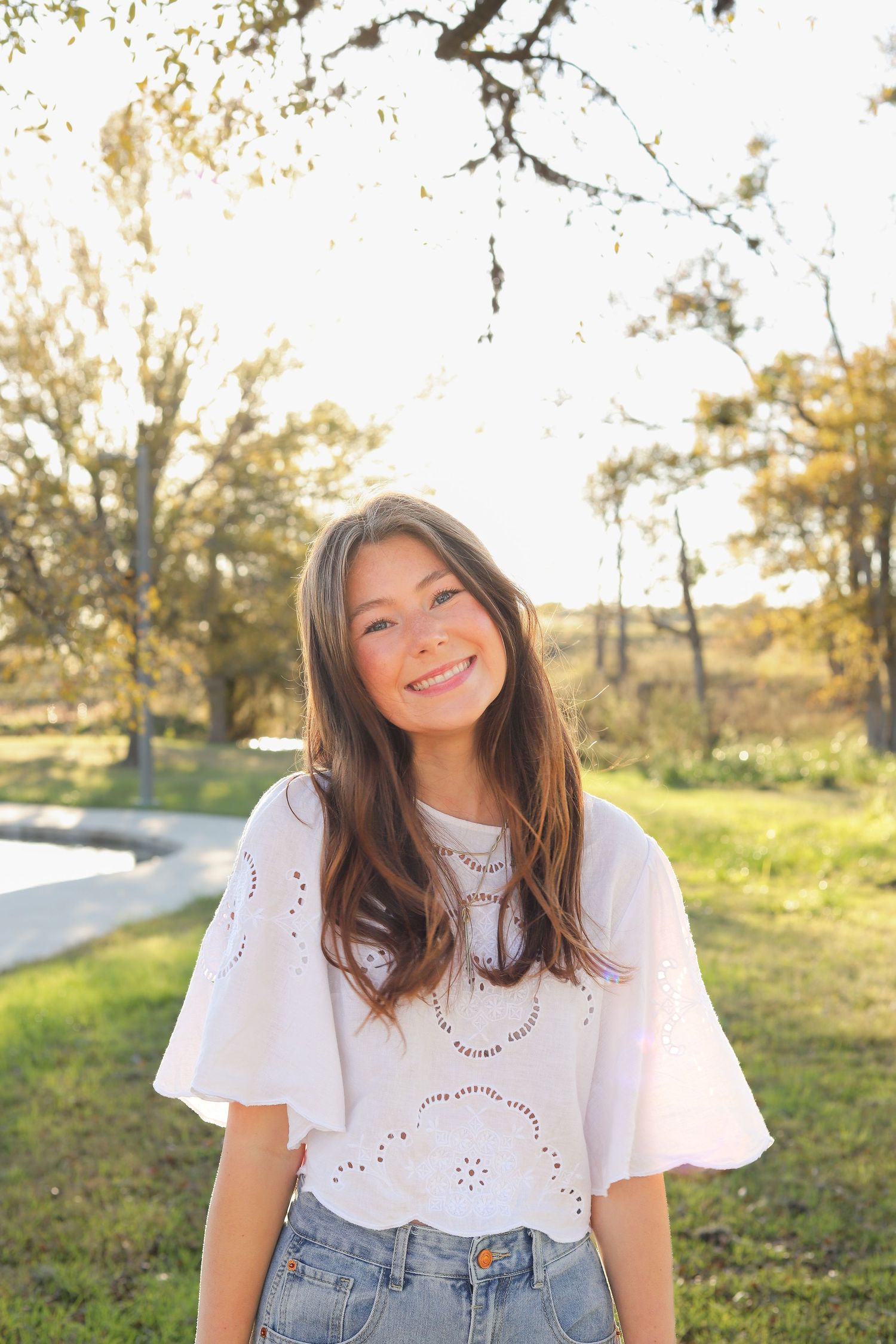 Casual outdoor photoshoot in white eyelet top and jeans during golden hour.