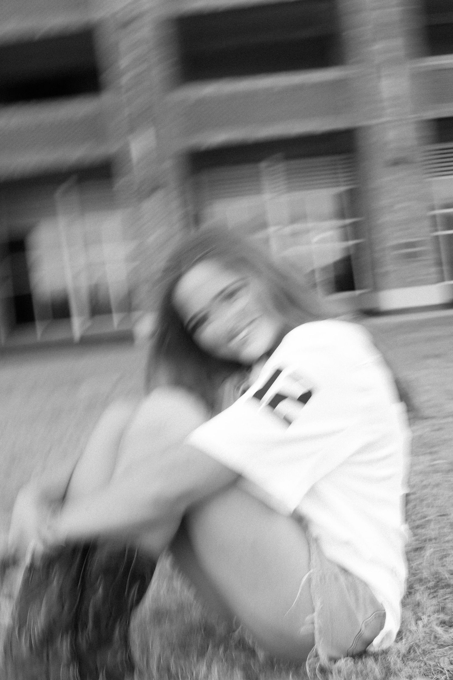 Motion blurred photo of person in white jersey lying on grass near brick building.