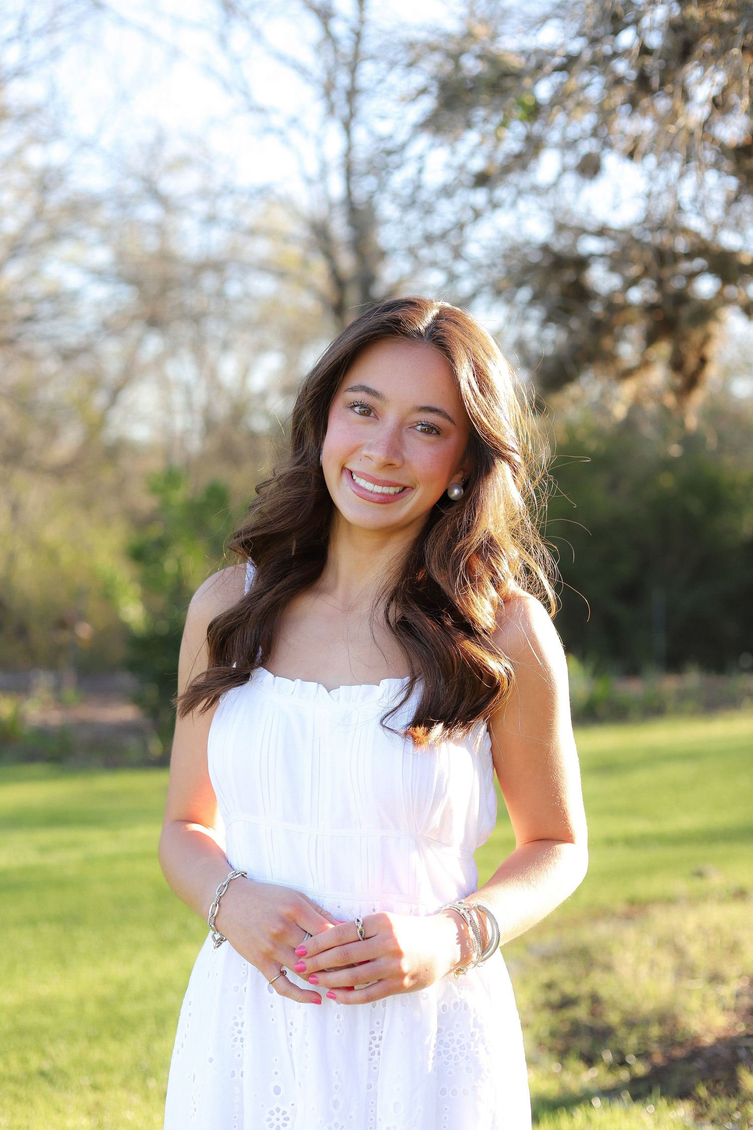 A person wearing a white eyelet dress stands in a grassy field during golden hour.