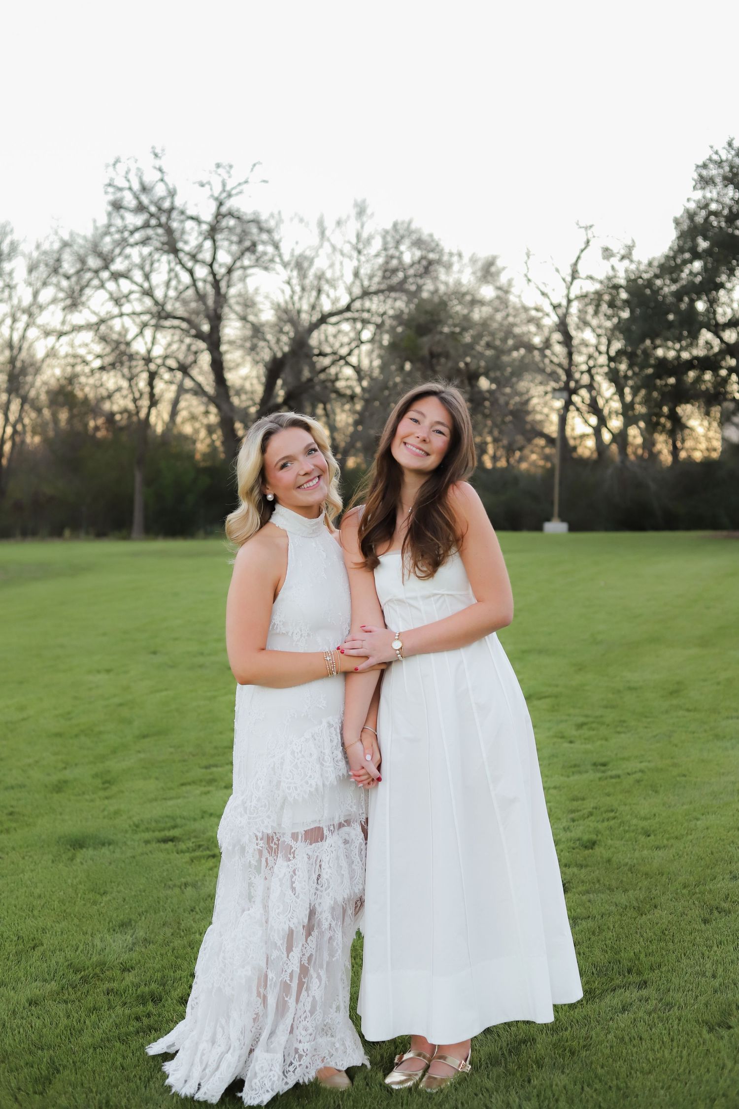Friends in white lace dresses share genuine laughter during an outdoor photo session.