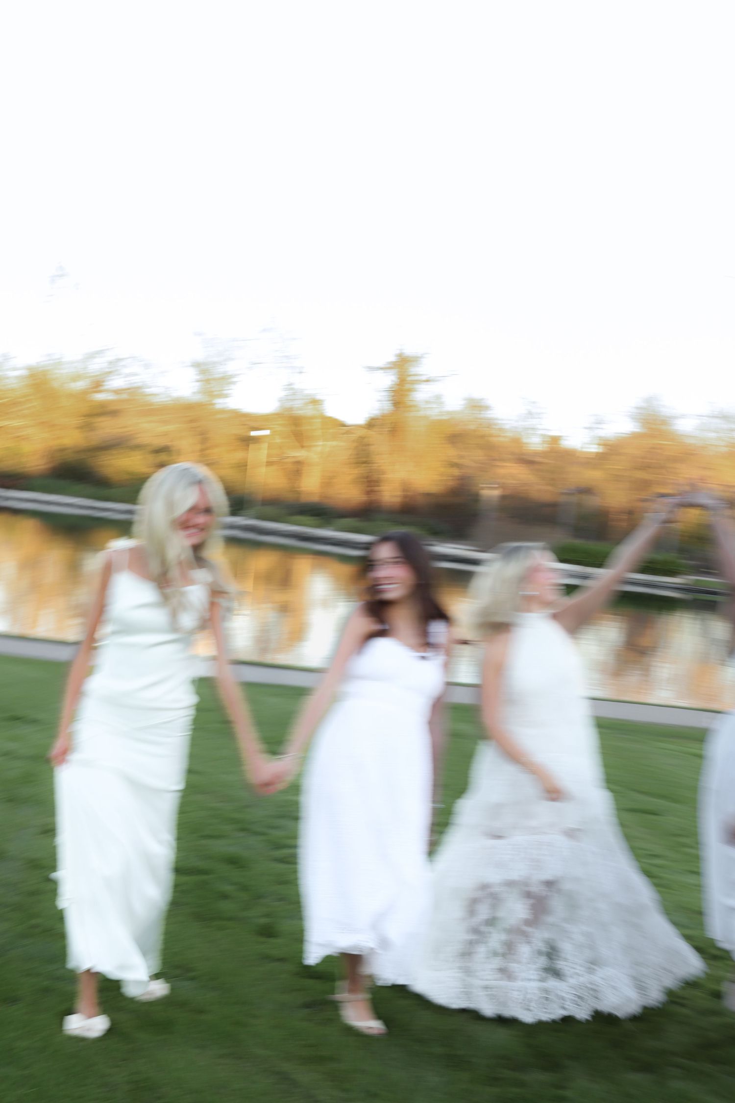 People in white dresses jump and dance together in a blurred motion shot outdoors.